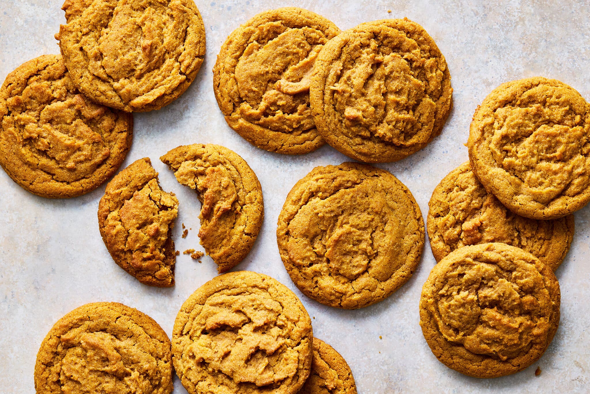 An overhead image of a dozen brown butter pumpkin cookies. One of the cookies is split in half.