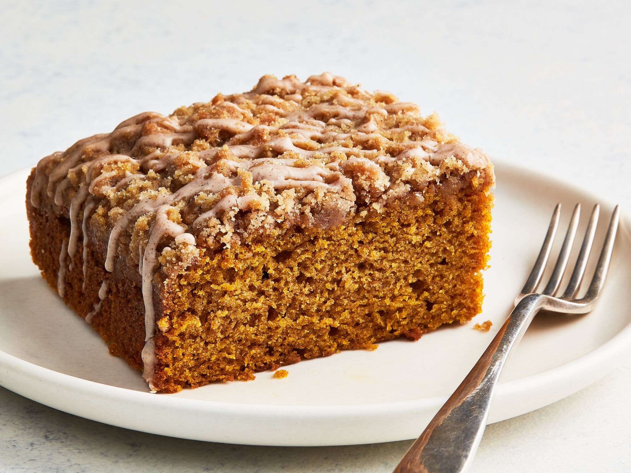 A side shot of a slice of pumpkin crumb cake with a pumpkin-spice drizzle.