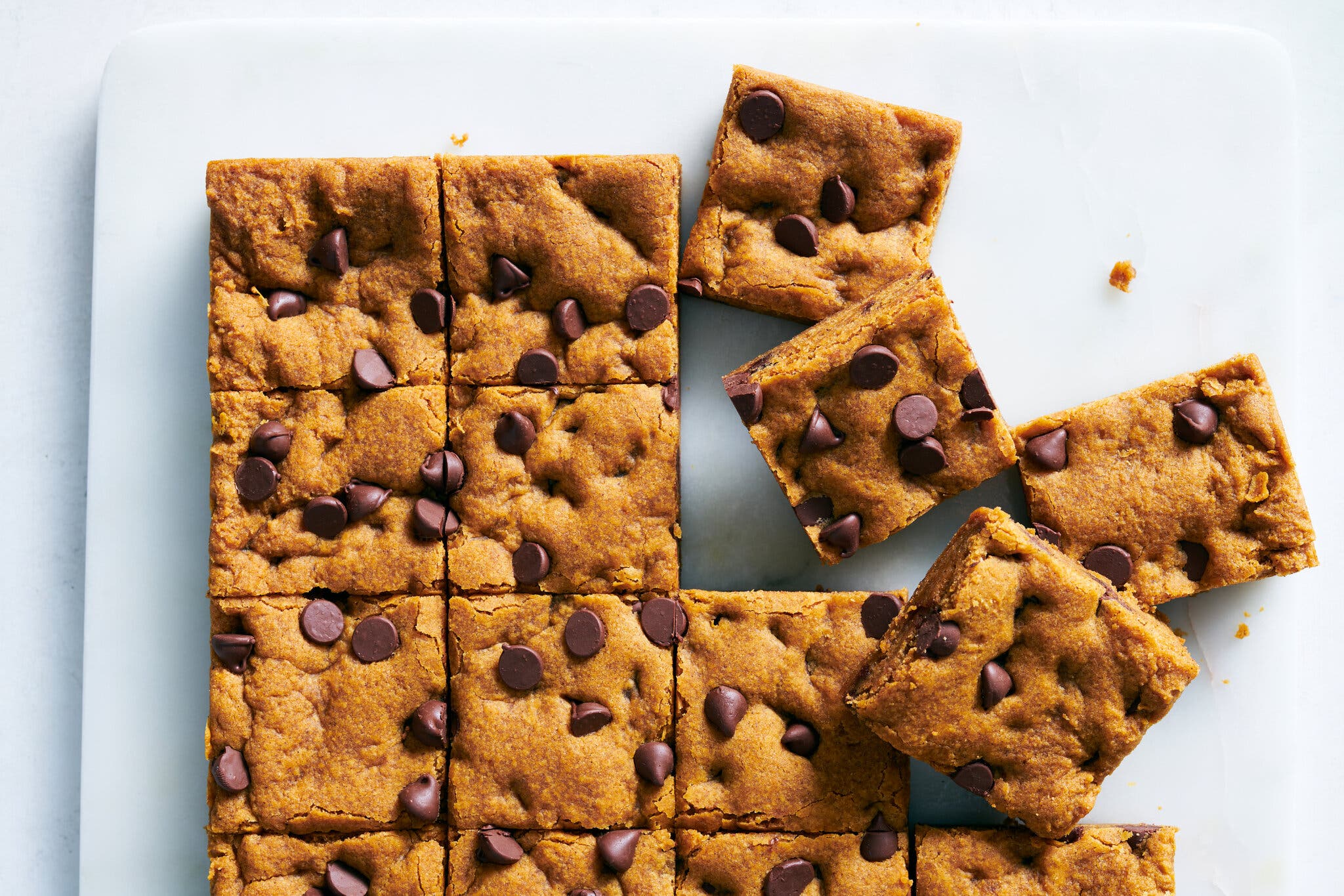 An overhead image of pumpkin chocolate chip cookie bars sliced into squares on a white cutting board.