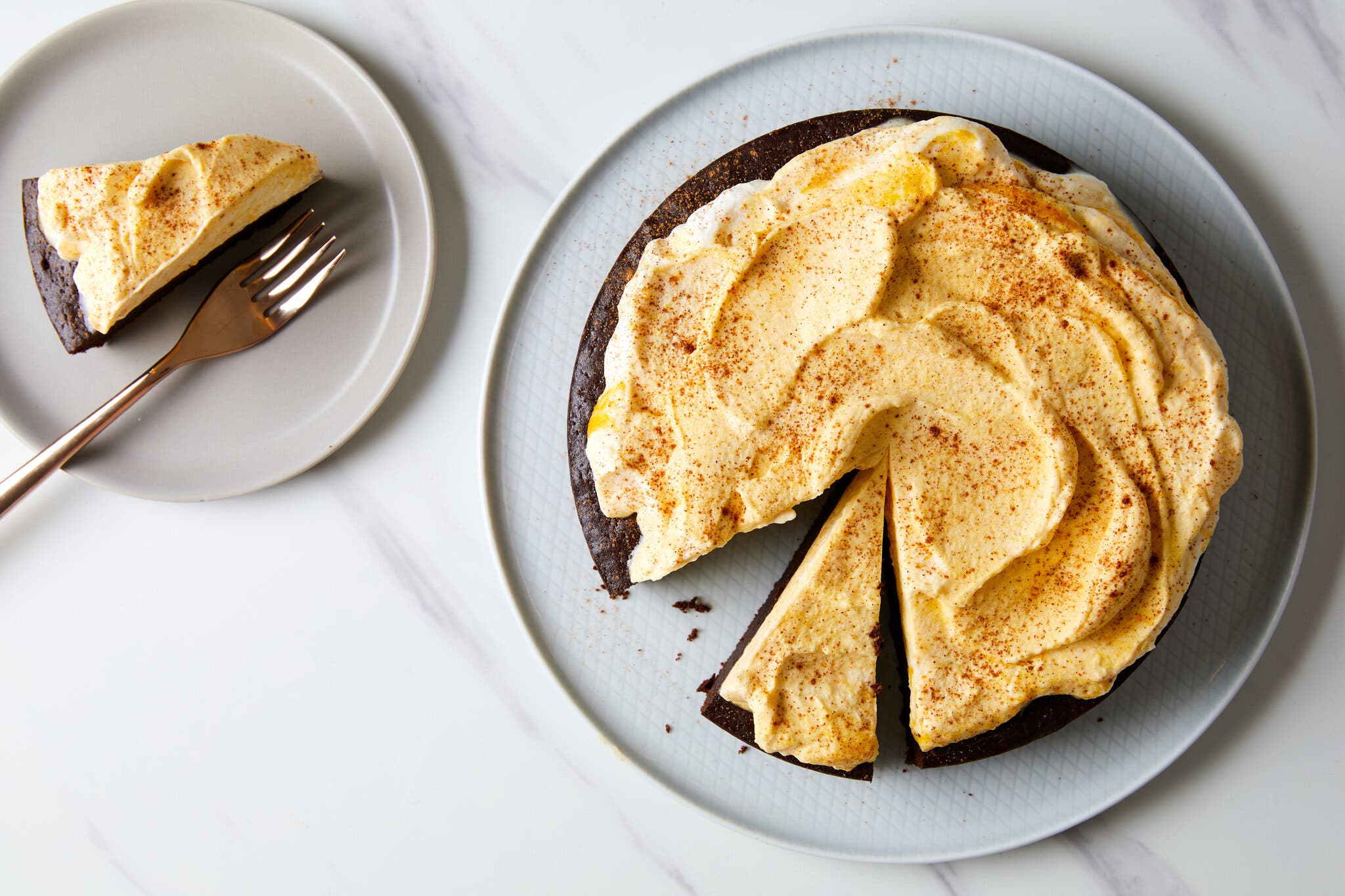 An overhead image of a pumpkin fudge torte with whipped cream topping. Two slices of cake have been cut. To the left is a slice of cake on a small plate with a fork.