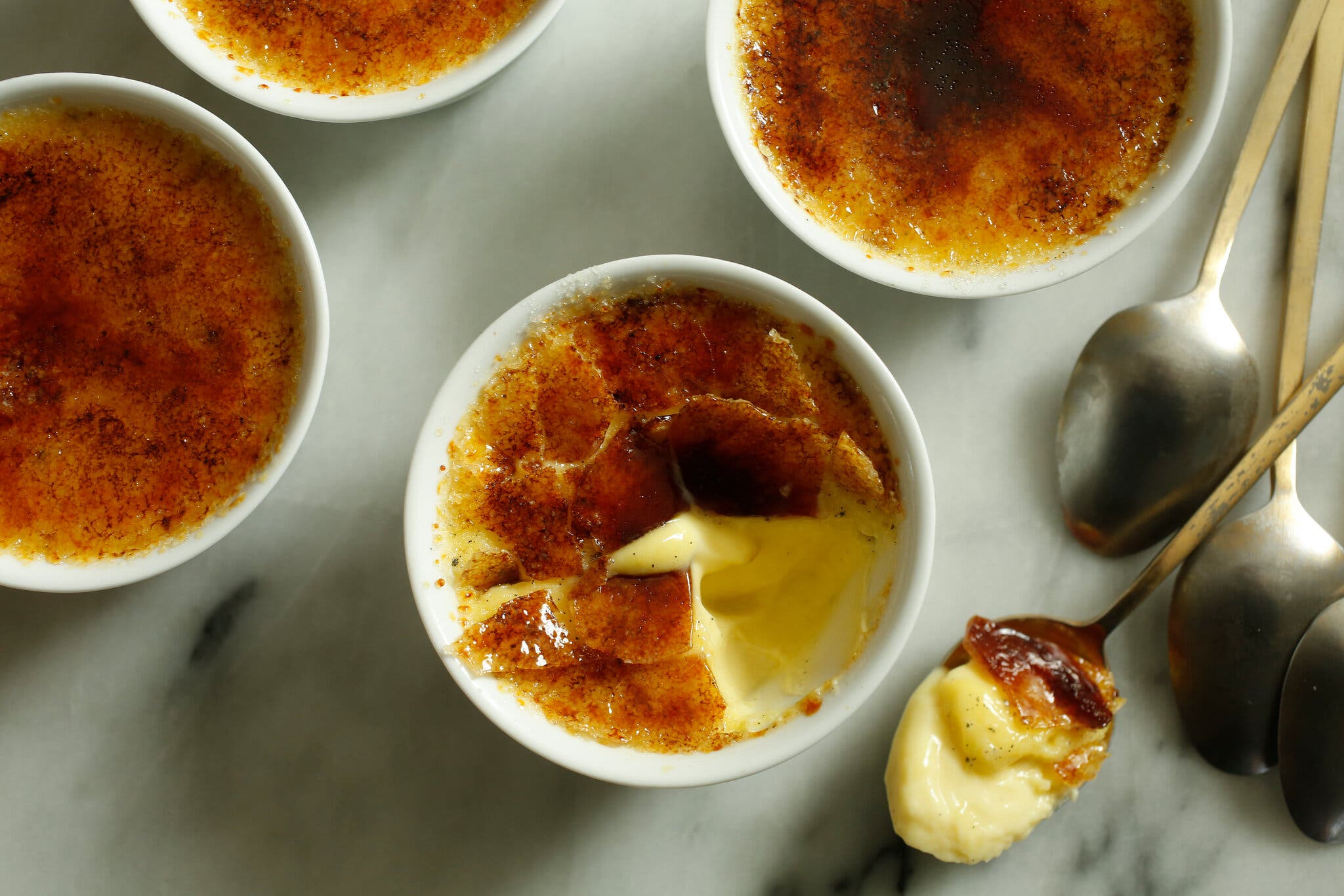 An overhead image of cups of crème brûlée. The one in the center has been cracked.