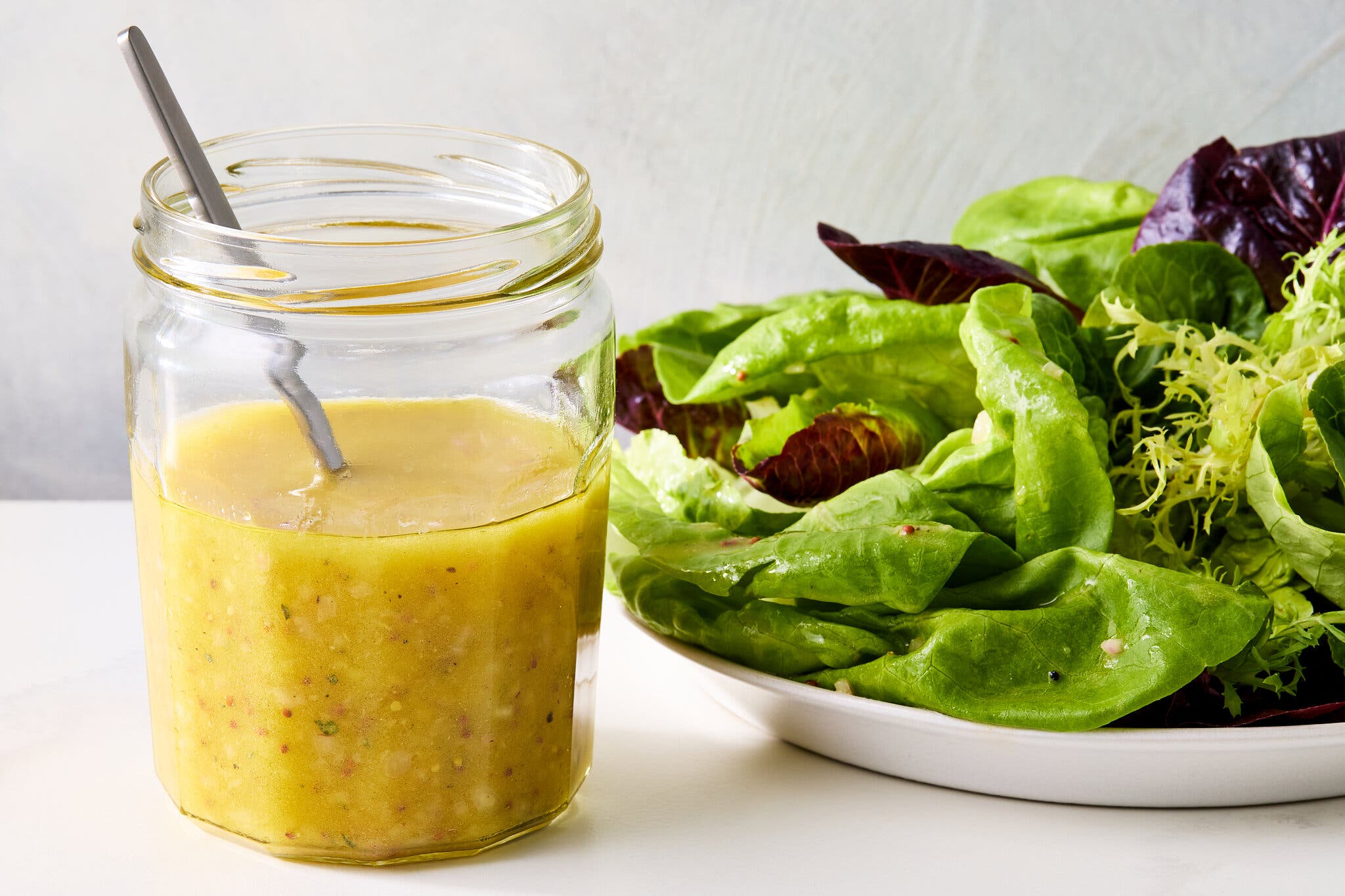 A side image of a jar filled with a golden dressing next to a green salad.