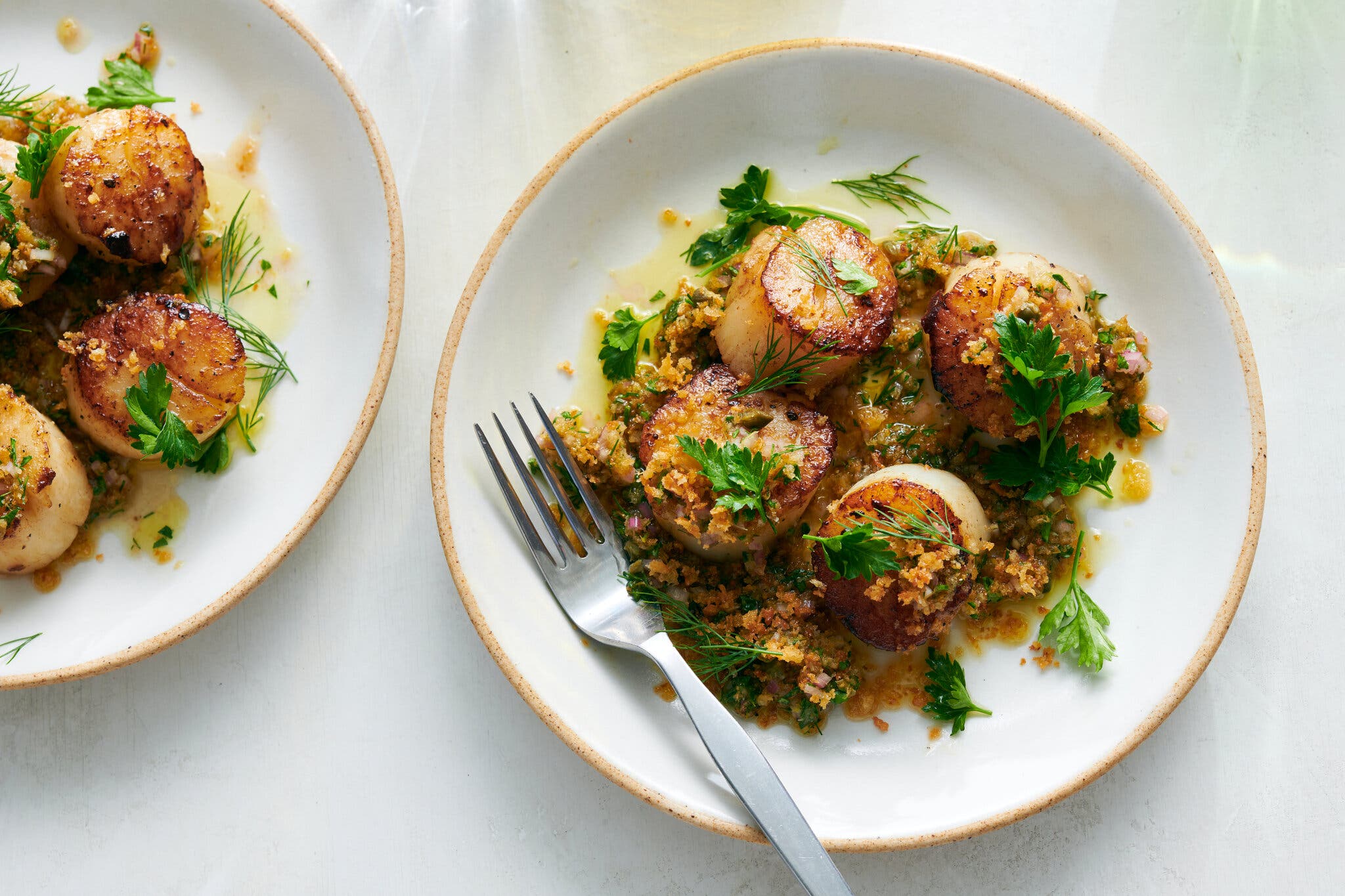 An overhead image of two plates of scallops with bread-crumb salsa verde.
