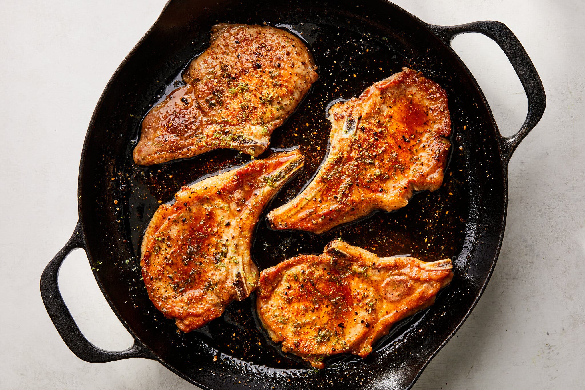 An overhead image of a skillet with four maple-soy pork chops.