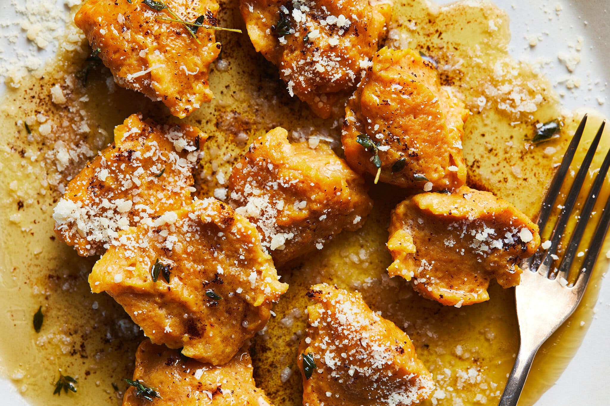 A close-up overhead image of pumpkin dumplings with brown butter and Parmesan.