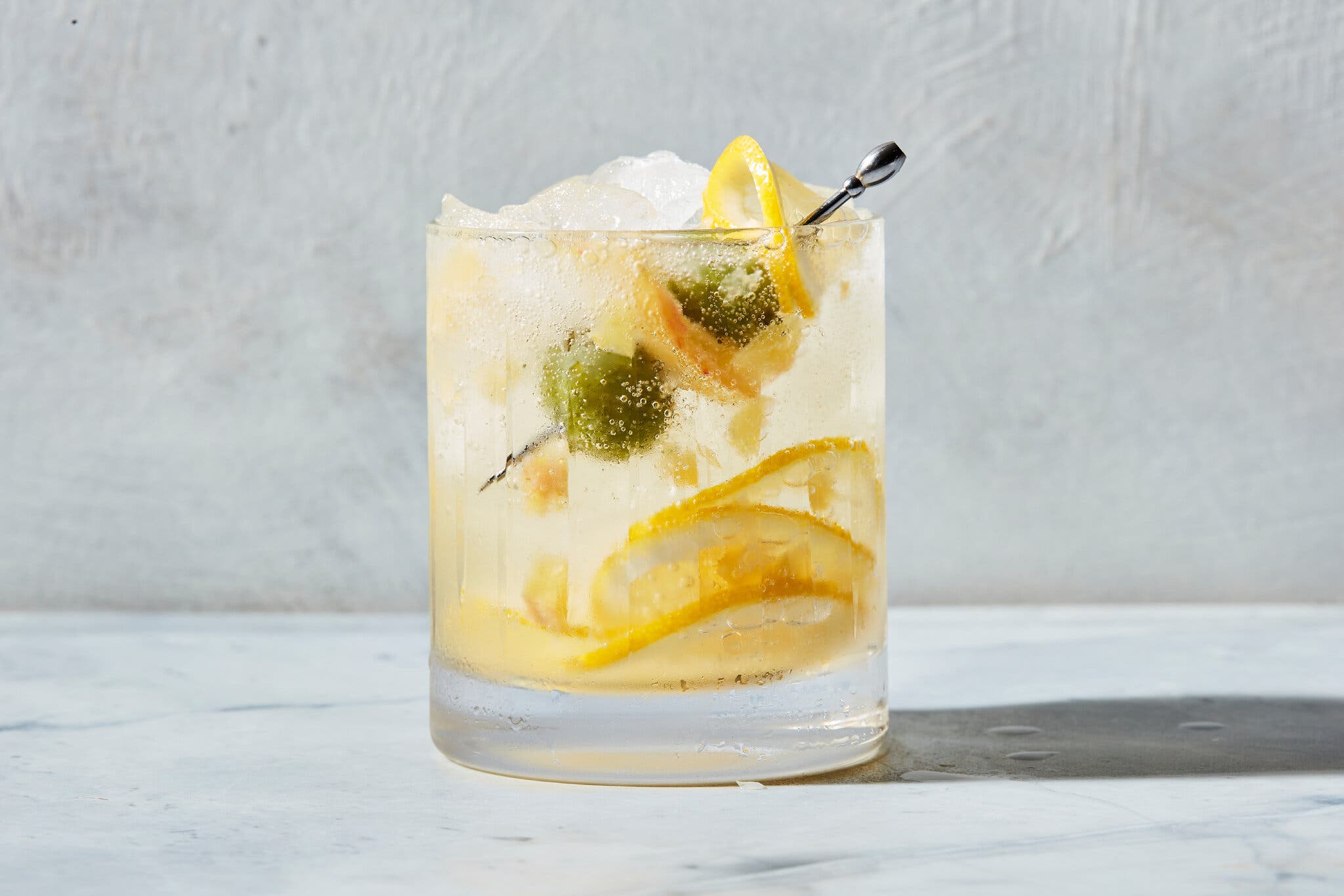 A side image of a nonalcoholic dirty lemon tonic in a tumbler glass with a lemon and olive garnish.