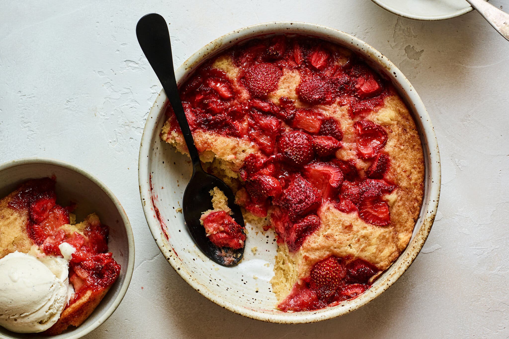An overhead image of strawberry spoon cake. In the bottom left corner there’s a bowl with a serving of cake and vanilla ice cream.