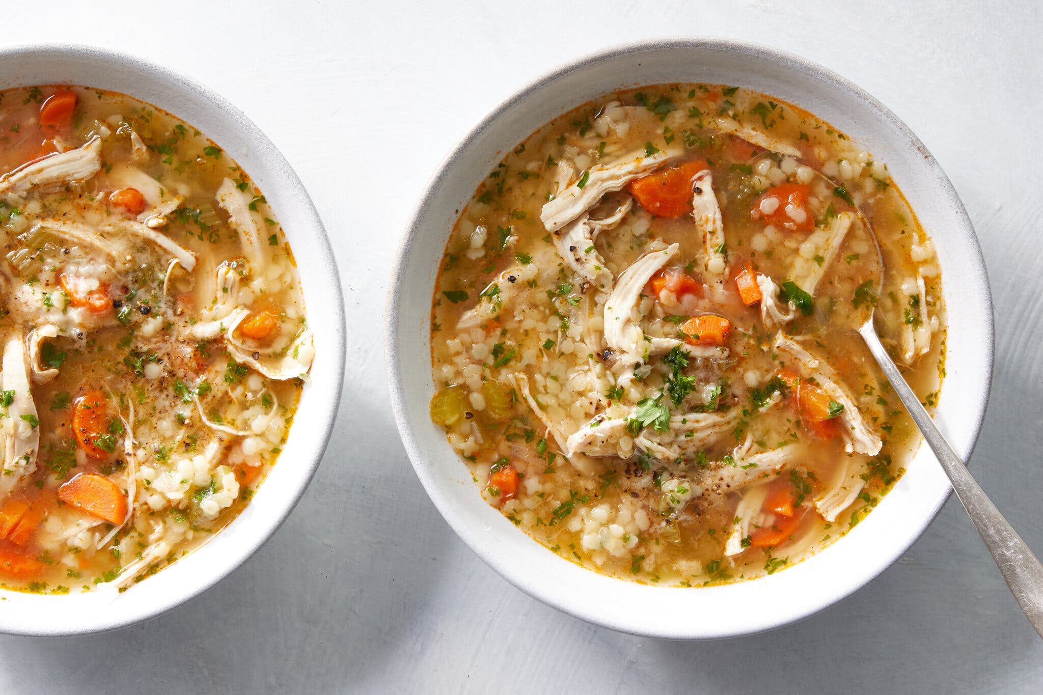 An overhead image of a bowl of pastina soup with parsley and carrots and shredded chicken. There is a spoon in the bowl.