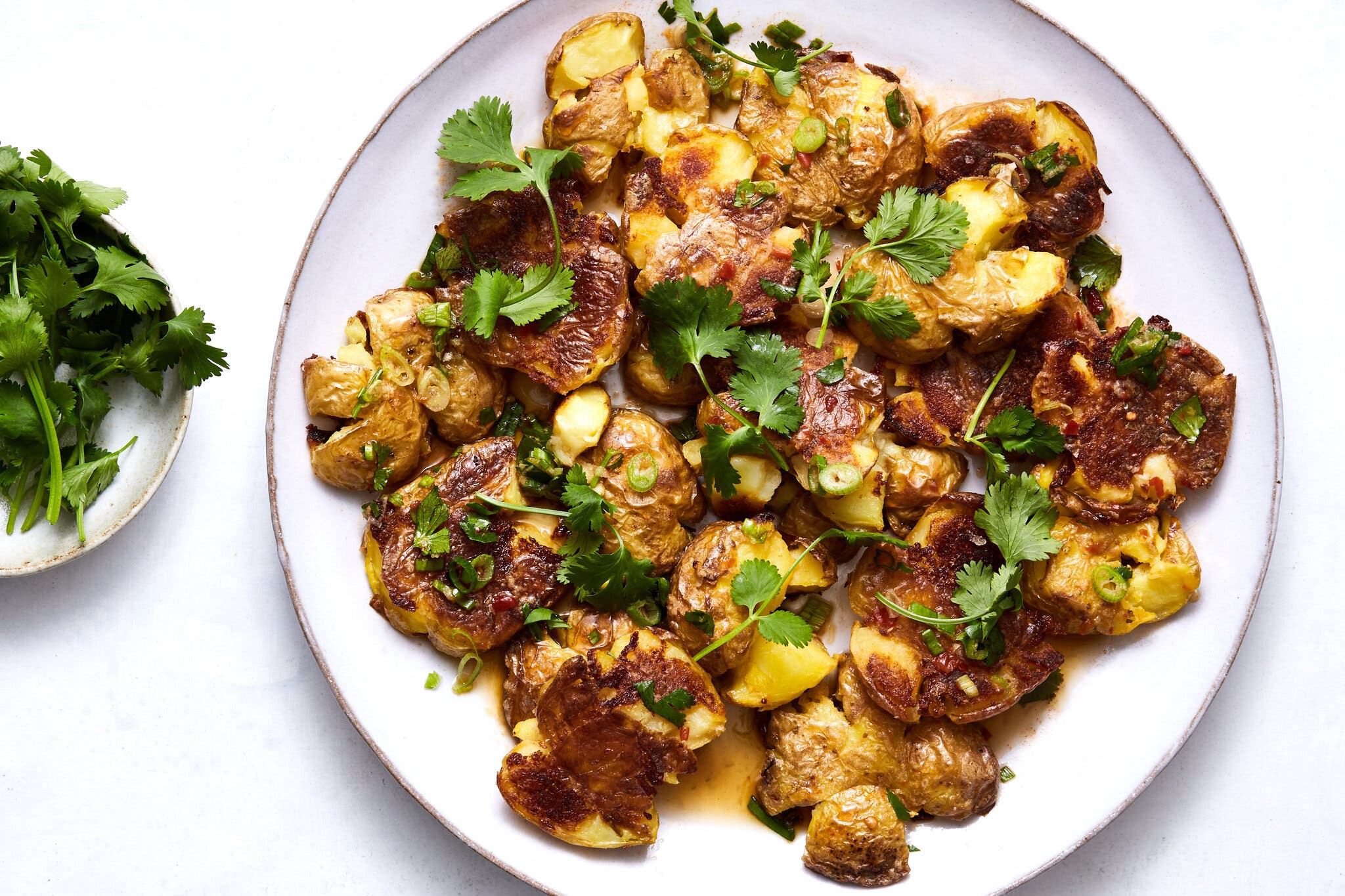 An overhead shot of a plate of smashed potatoes with a Thai-style chile and herb sauce, garnished with fresh cilantro and scallions.