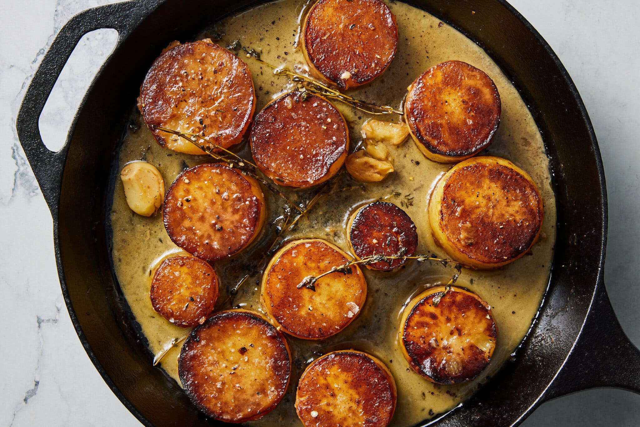 An overhead image of a cast iron skillet with fondant potatoes.