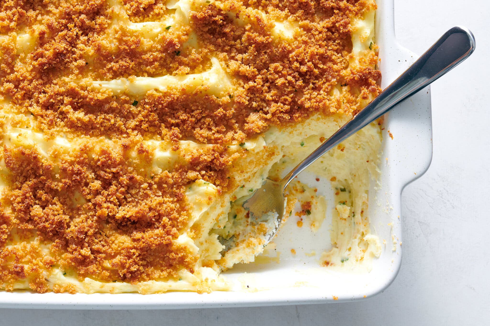 An overhead image of a mashed potato casserole topped with golden brown bread crumbs with a scoop taken out. 