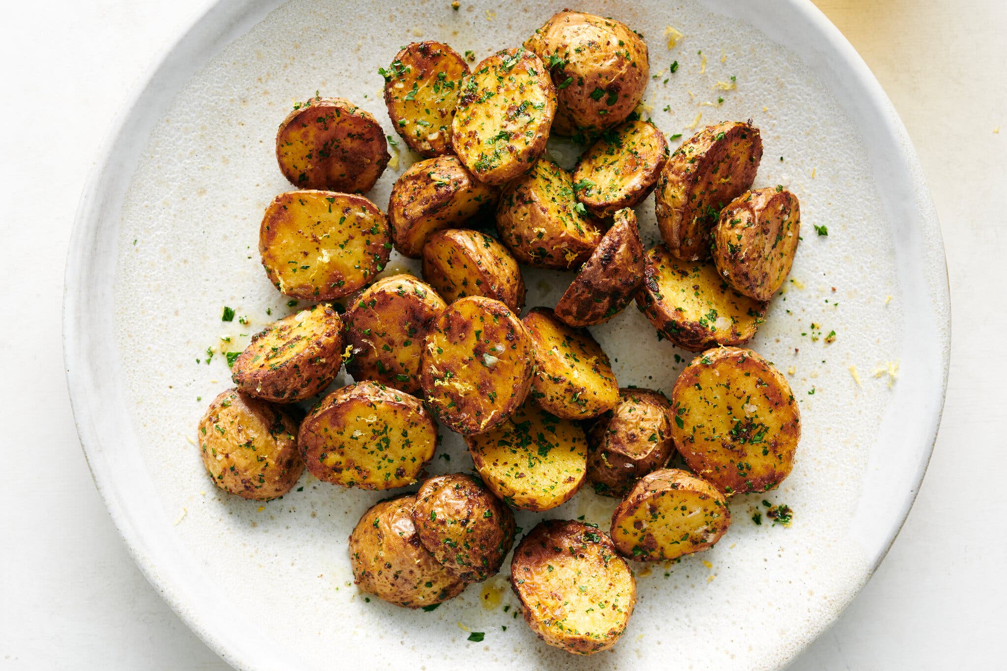 An overhead image of air-fryer potatoes with dried parsley on a white plate.