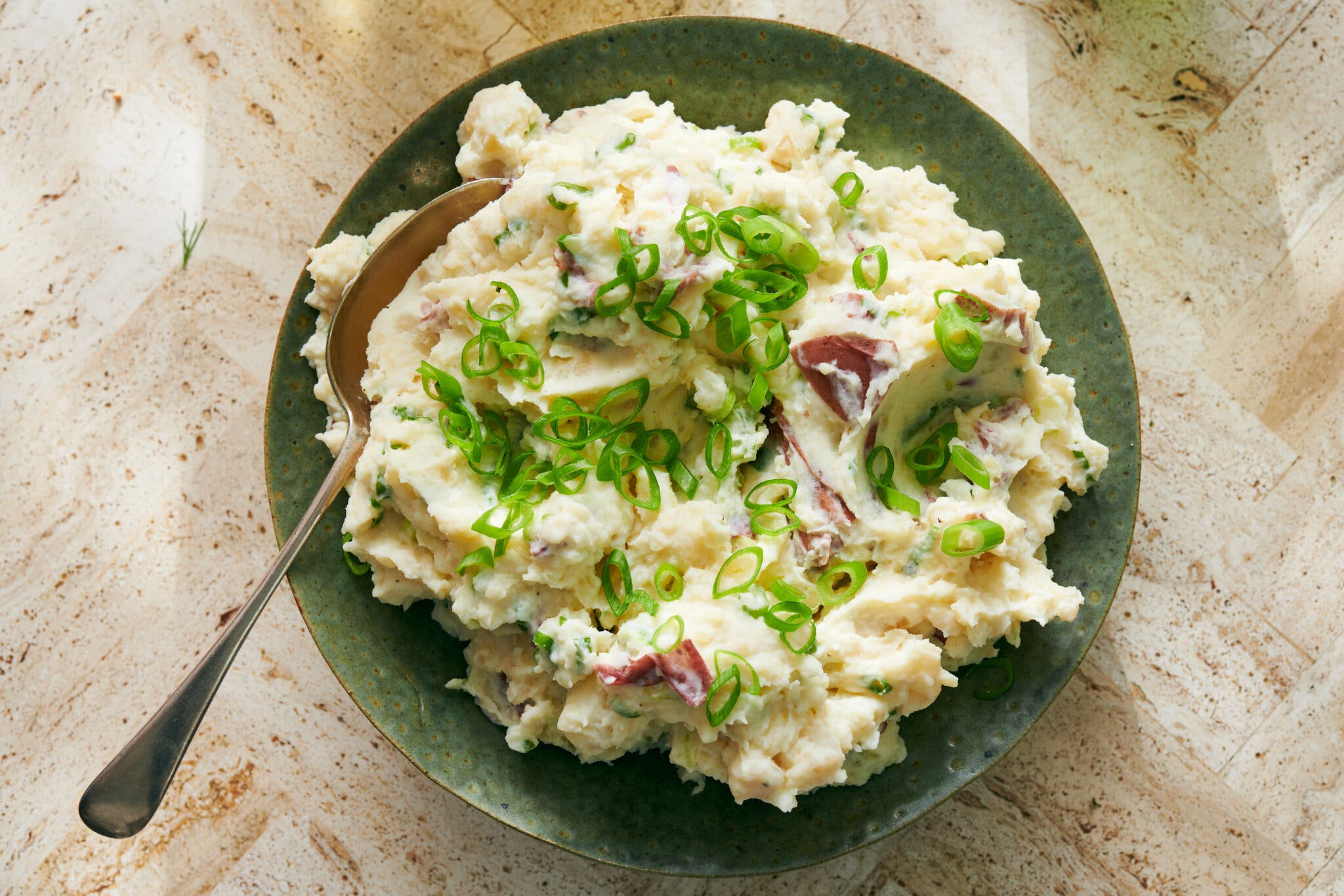 An overhead image of mashed potatoes scattered with sliced scallions.