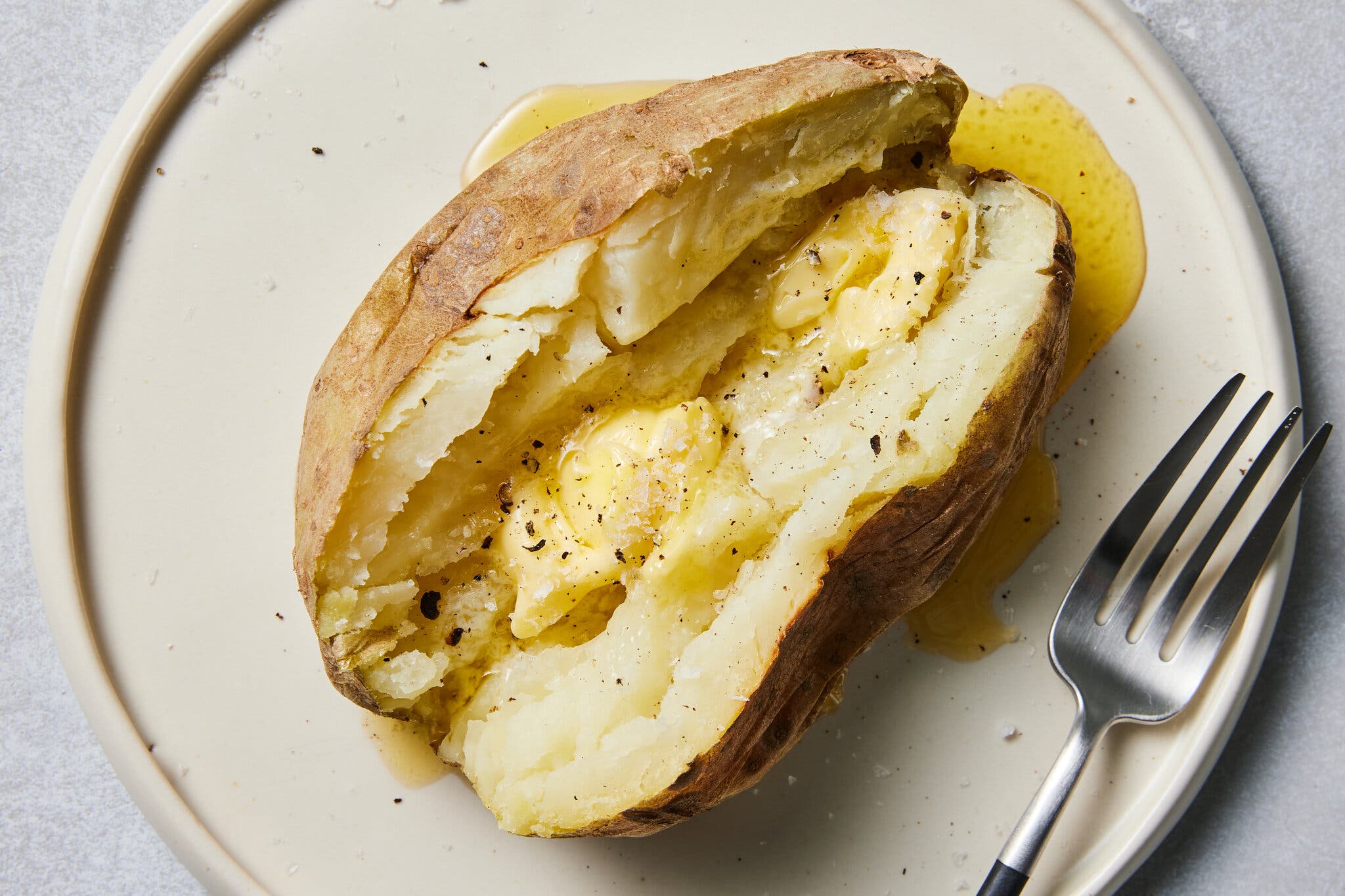 An overhead image of a baked potato sliced down the middle with butter inside and pooling at the edge.