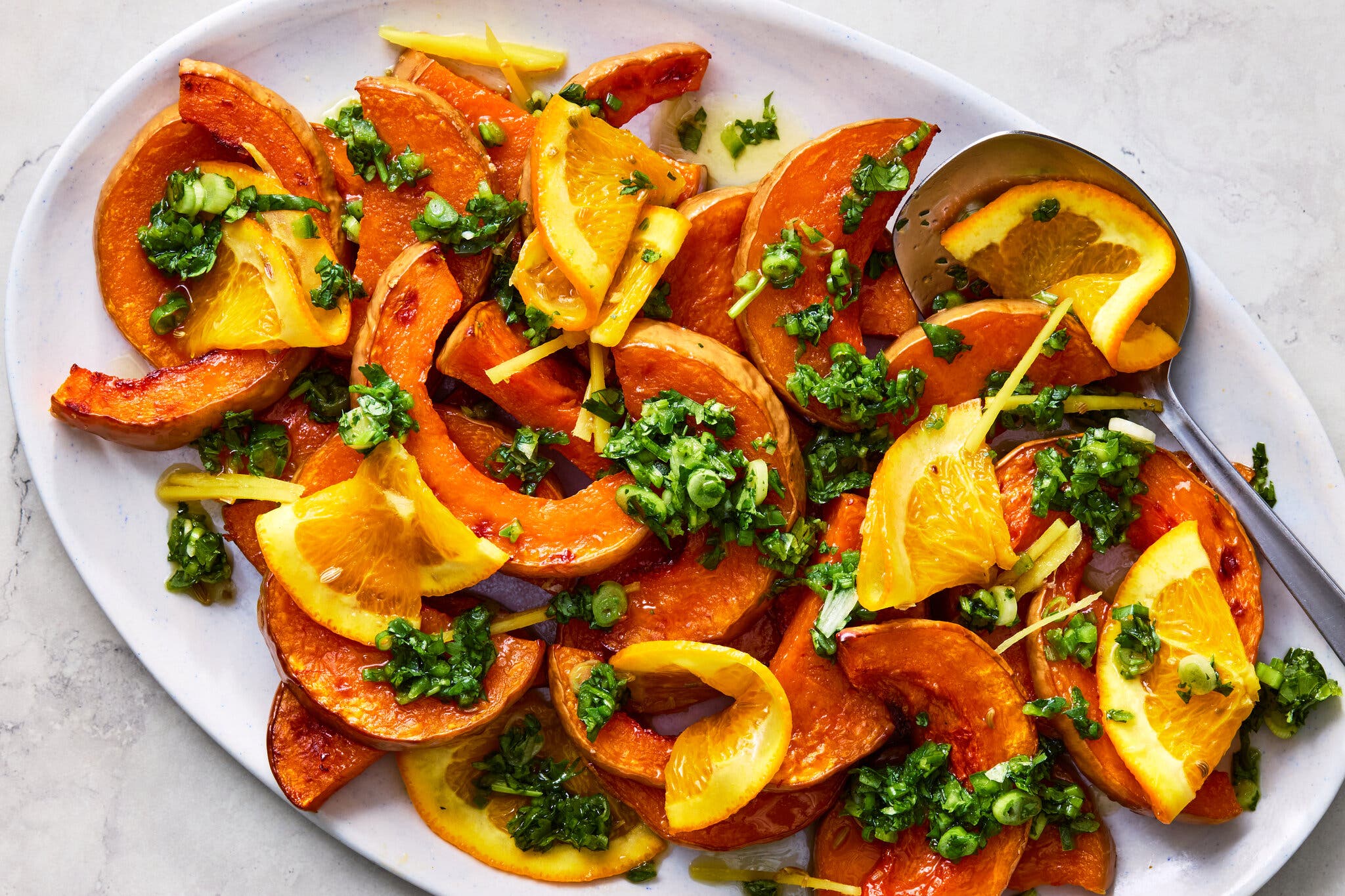 A white plate of roasted butternut squash salad topped with a green sauce. A metal spoon sits at the top right corner.
