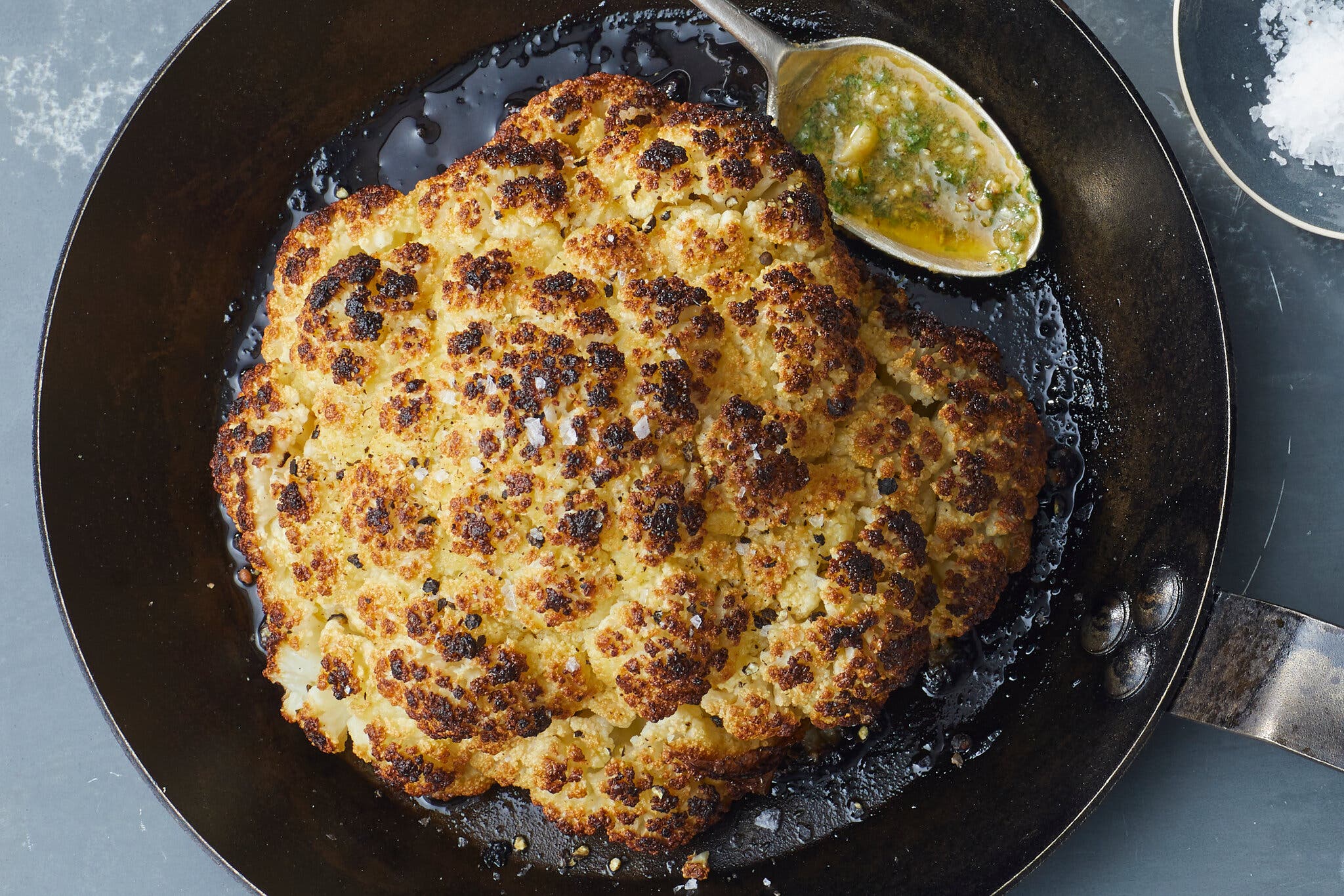 An overhead shot of a pan with whole roasted cauliflower. A spoon head sits at the top right corner of the pan.