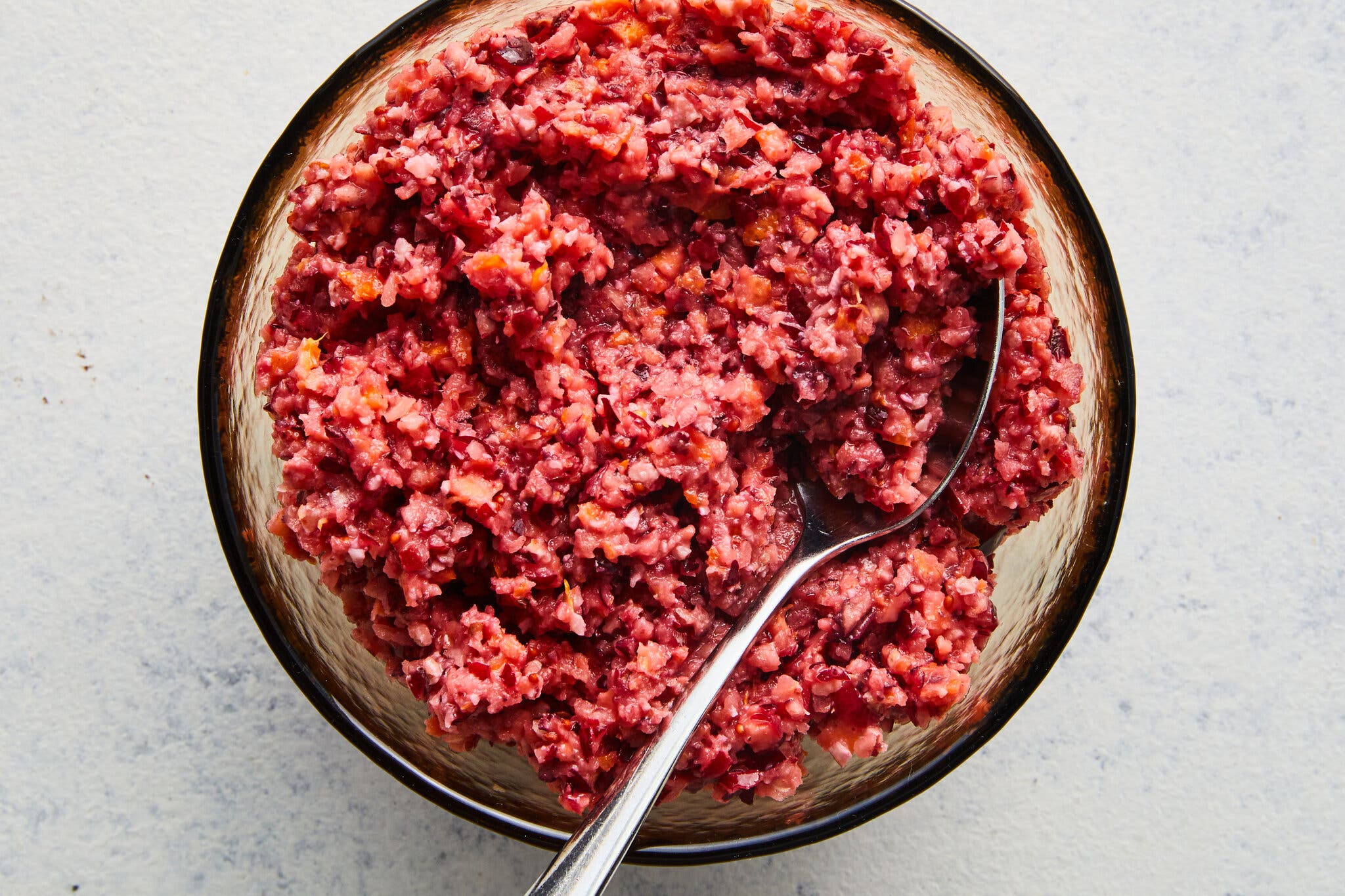 An overhead shot of a cranberry-orange relish in a bowl. A spoon sits at the right side of the bowl.