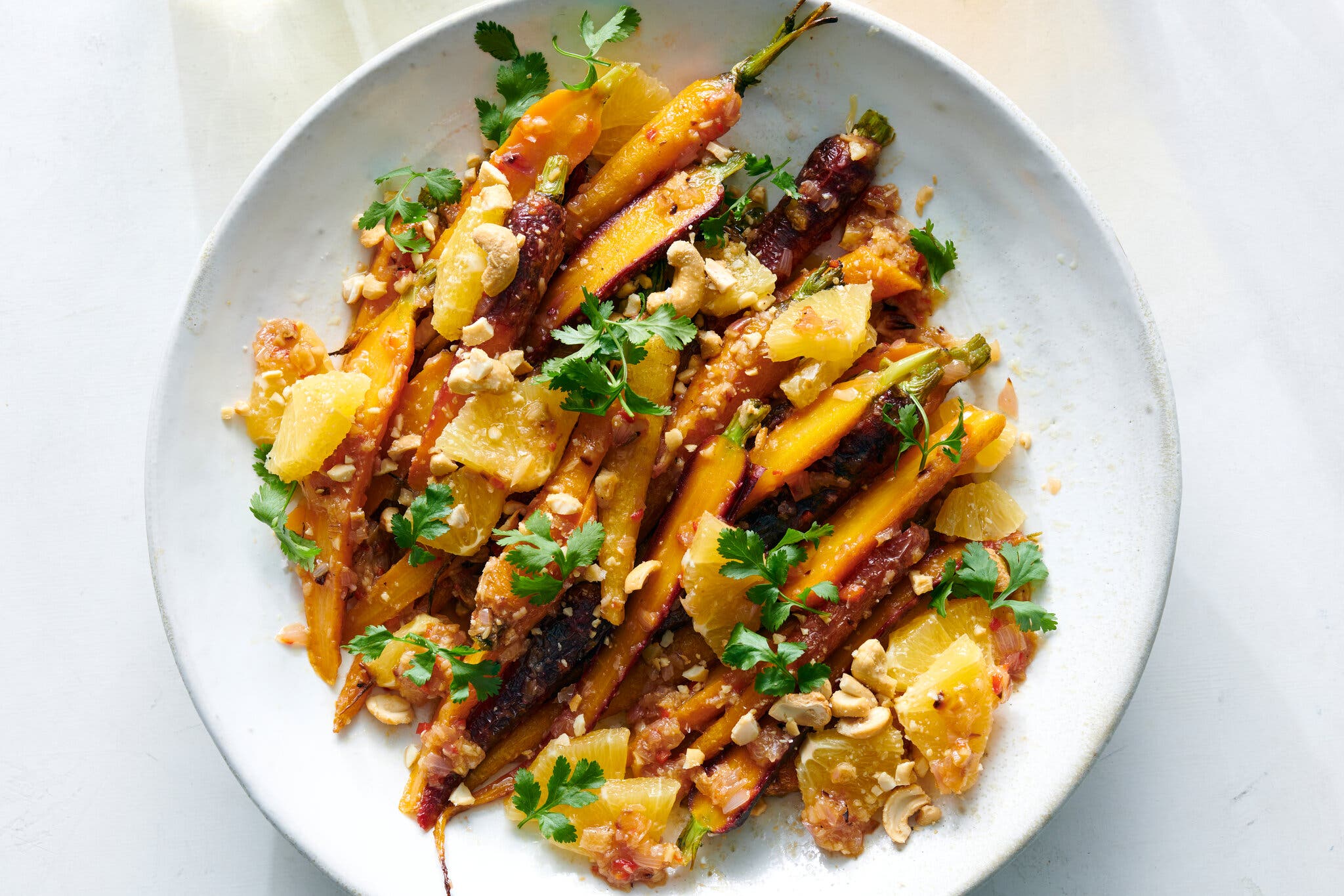 An overhead shot of a white plate of carrot salad with oranges and cashews topped with cilantro sprigs.