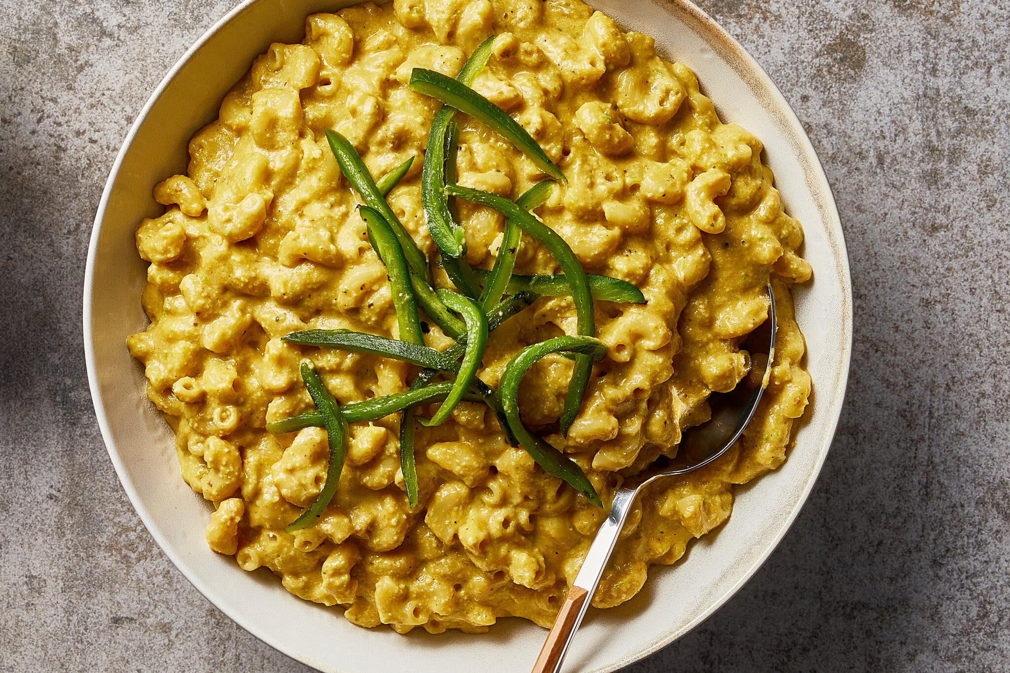 An overhead shot of a white plate of vegan poblano macaroni and cheese. A silver spoon juts out at the bottom right corner.