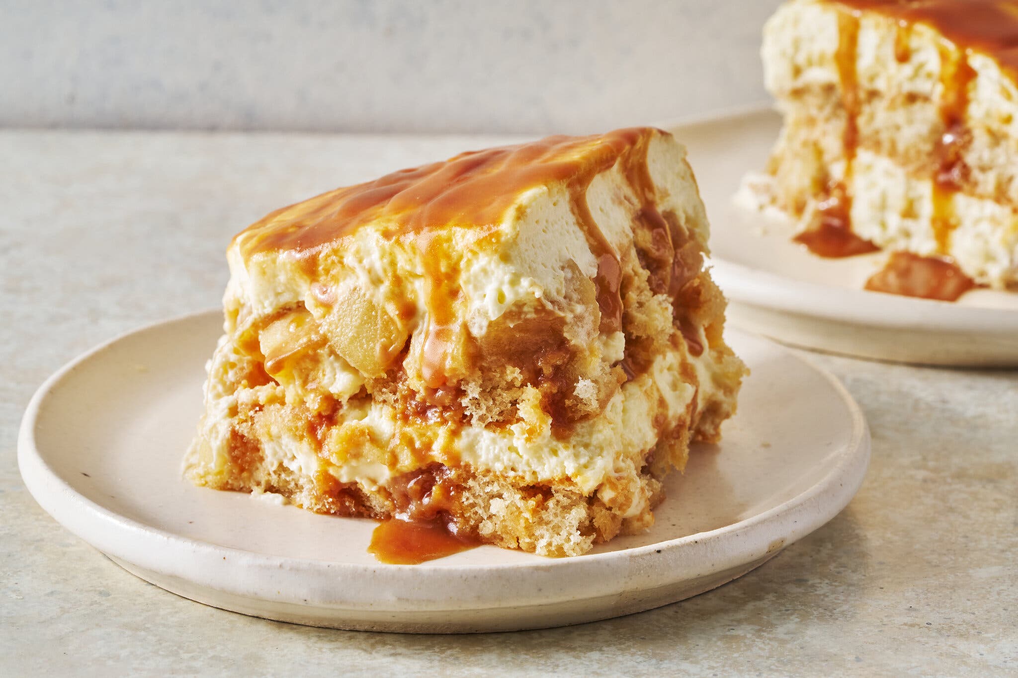 Two squares of apple tiramisù with caramel sauce sit on white stone plates.