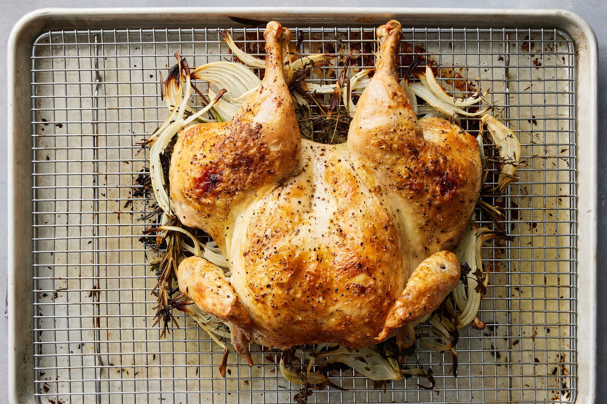 An overhead image of a spatchcocked chicken on a rack set into a rimmed sheet pan.