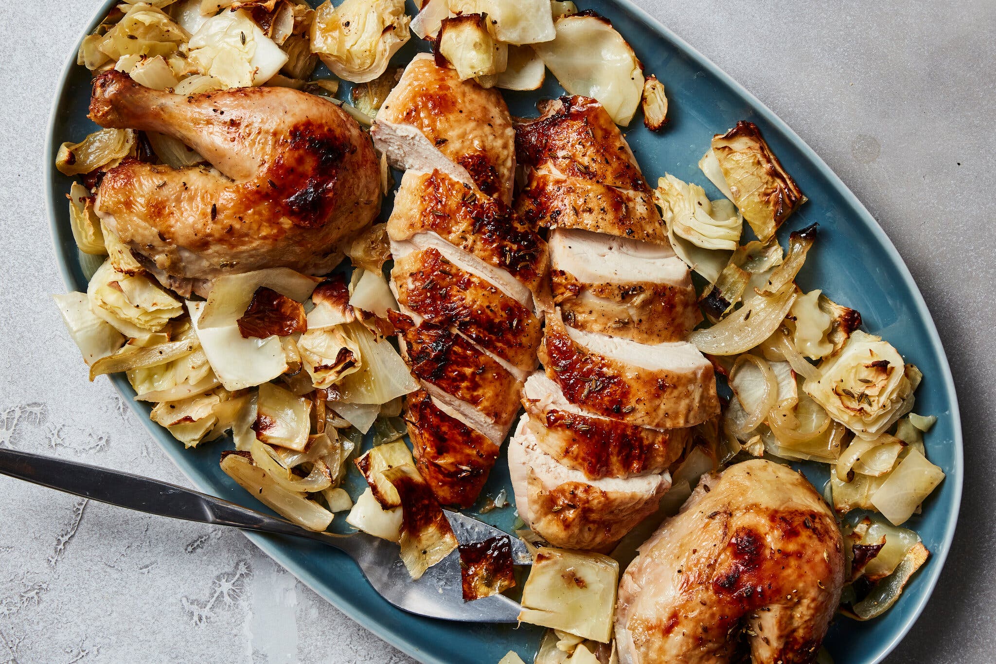 An overhead image of a carved chicken surrounded by roasted cabbage on a blue platter.