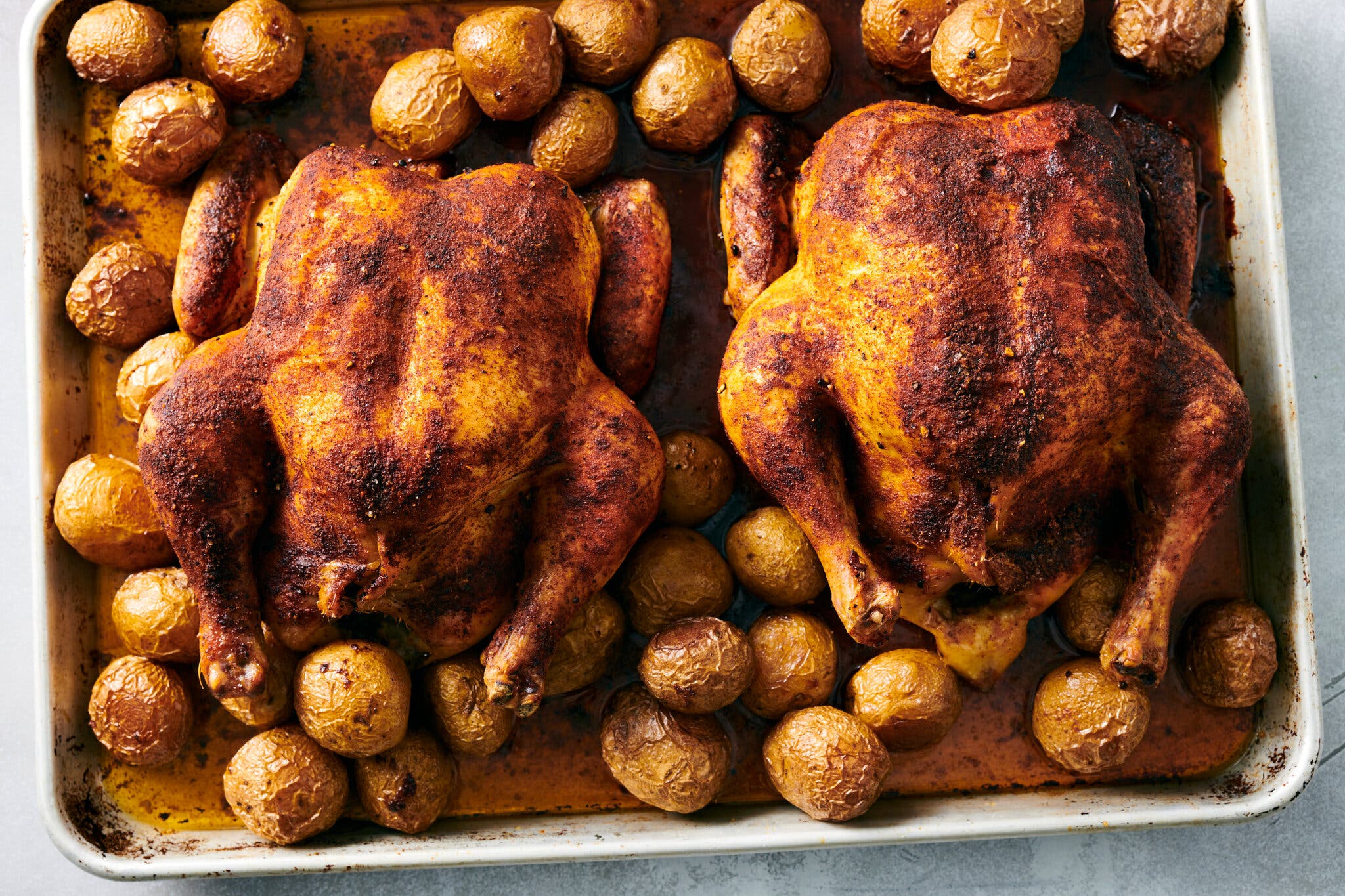 An overhead image of two whole roasted chickens surrounded by potatoes on a sheet pan.