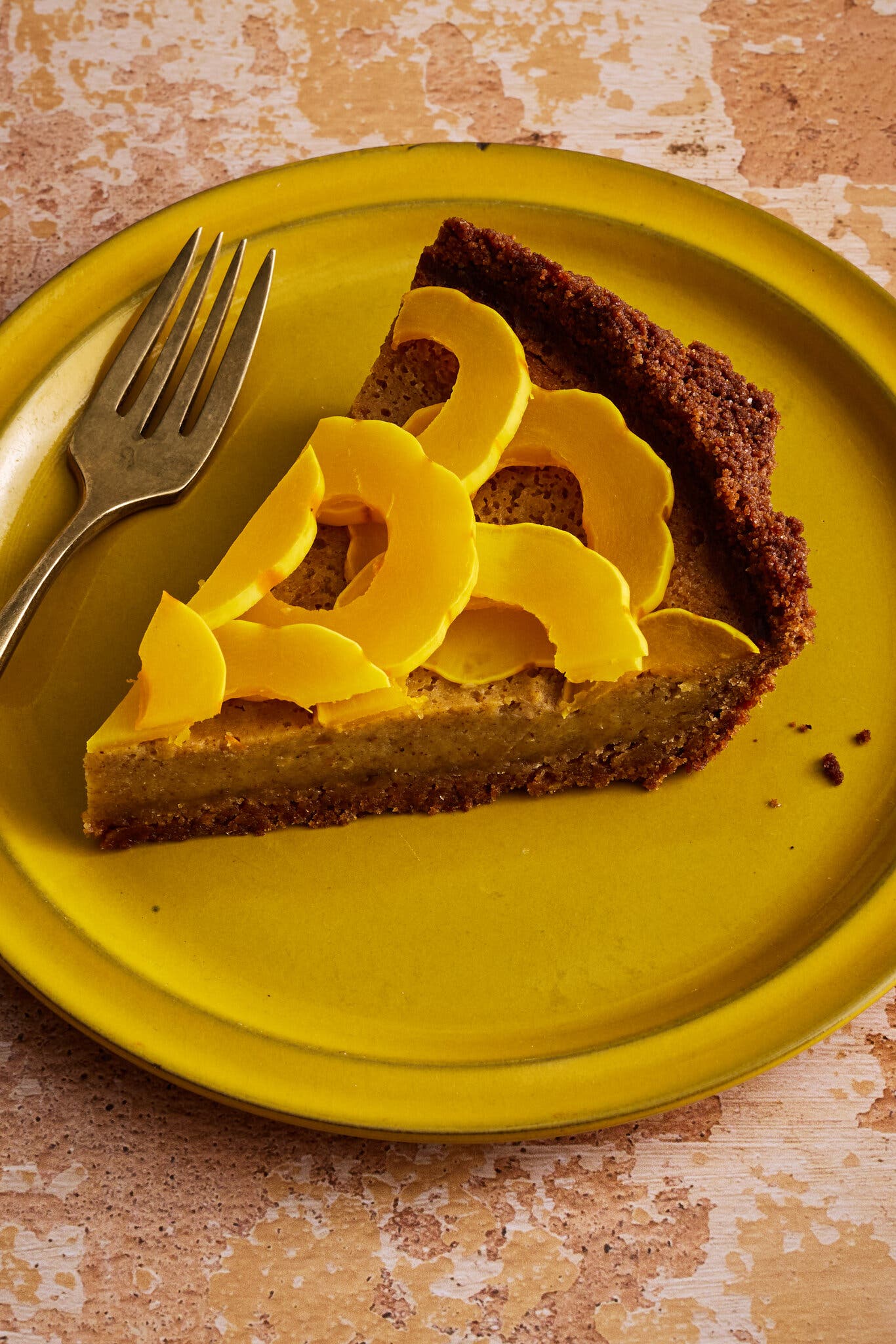 A slice of pie topped with rings of delicata squash sits on a yellow plate that has a fork resting on it.
