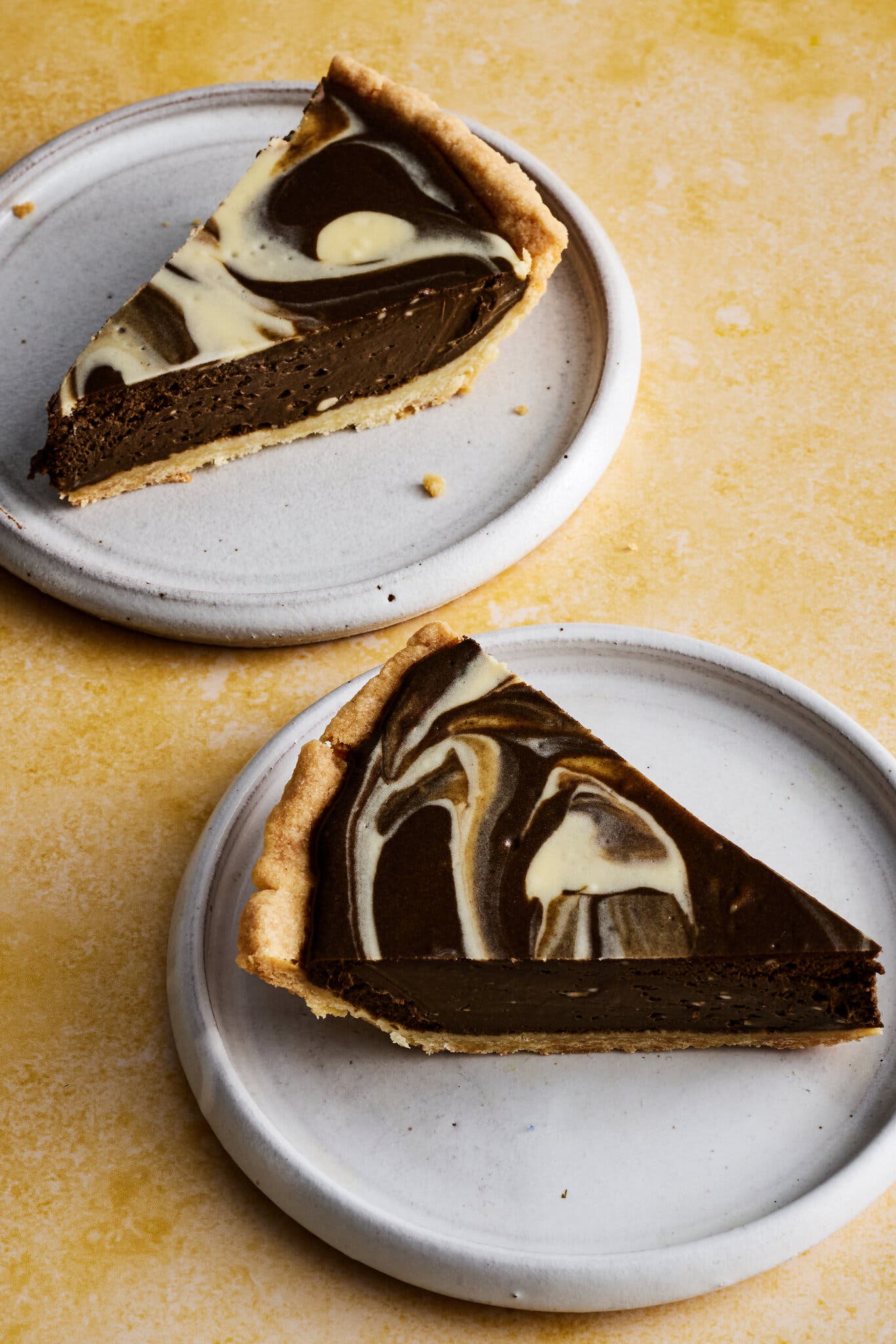 Two slices of pie with a swirled black and white top sit on white plates against a yellow background.