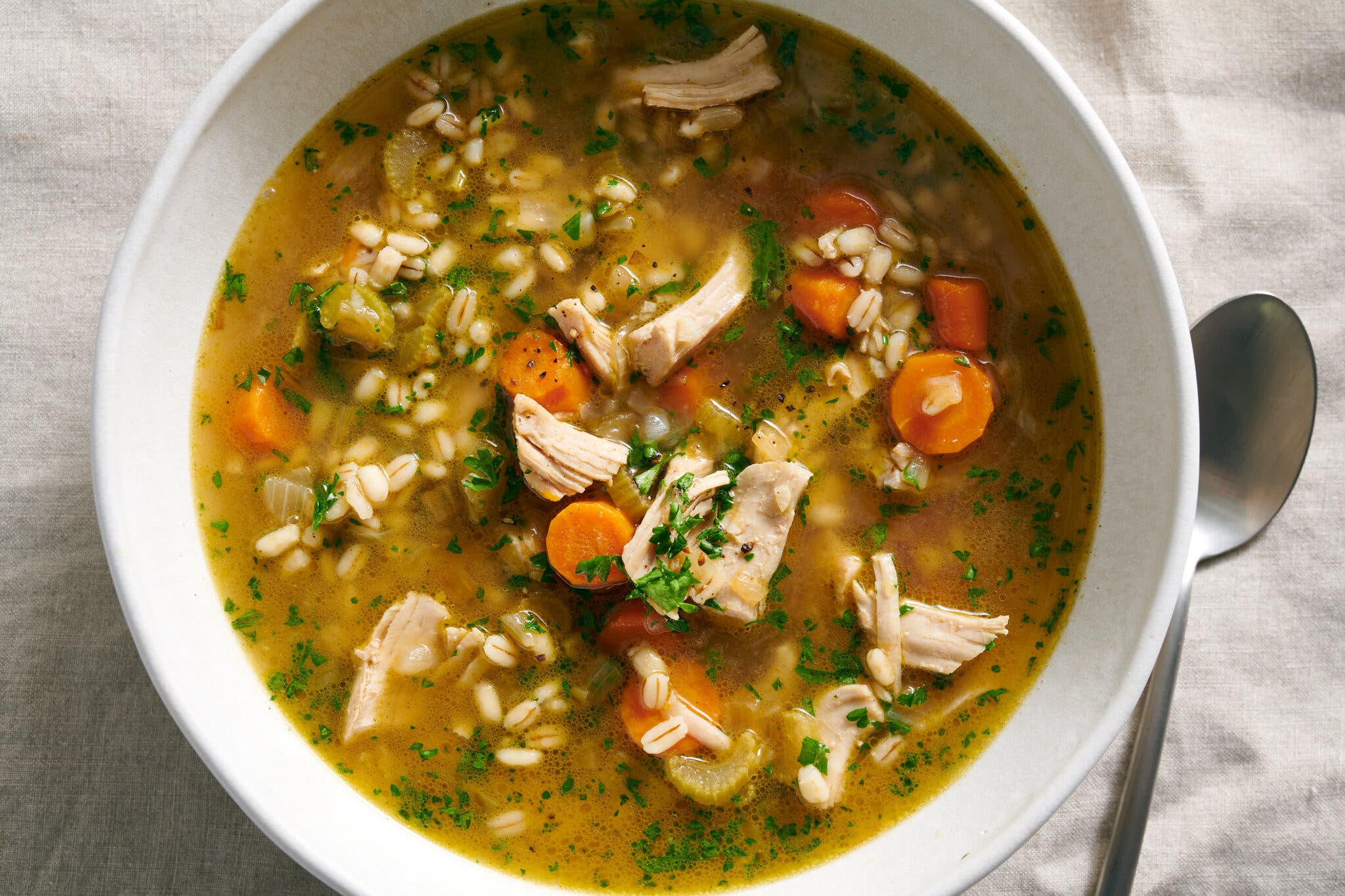 A bowl of golden soup with chunks of turkey, carrots, barley and green herbs. 