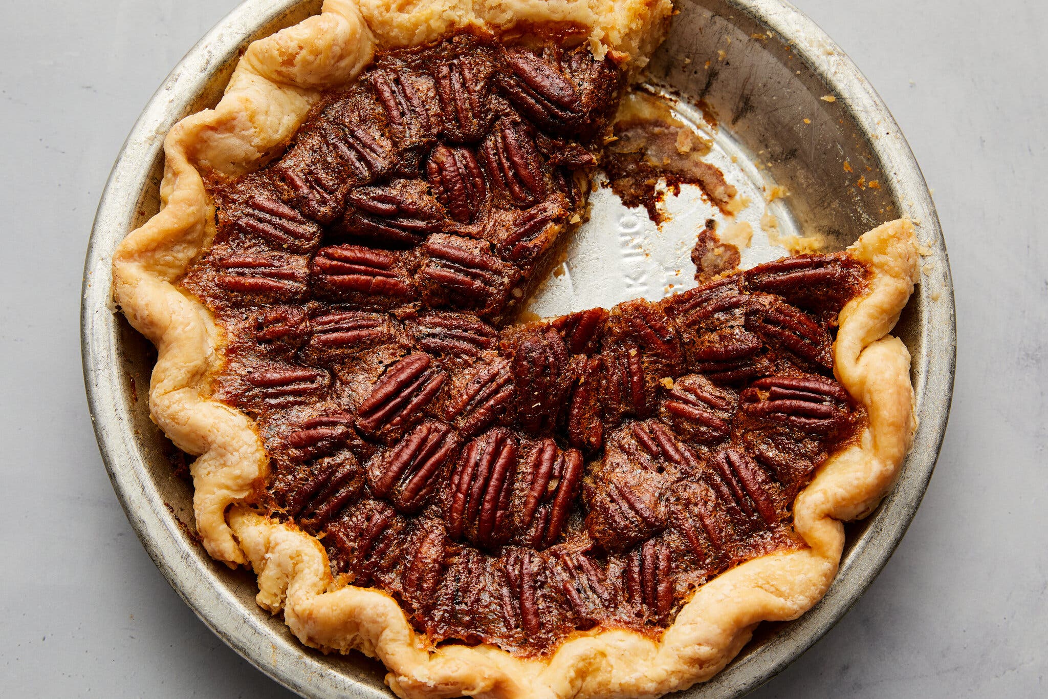 A round pecan pie in a metal dish with a slice missing.