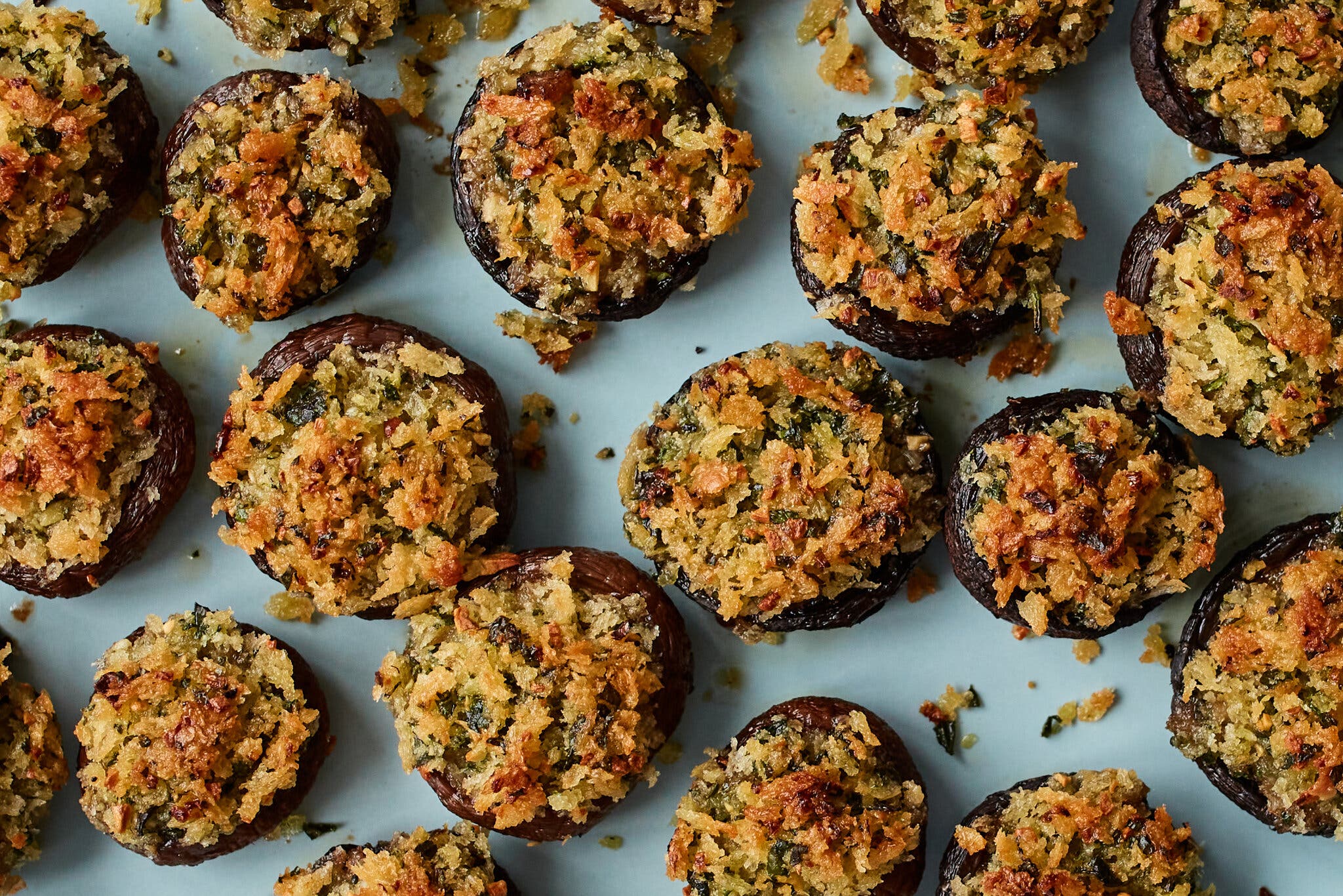 An overhead view of numerous stuffed mushrooms, each topped with golden, textured breadcrumbs.