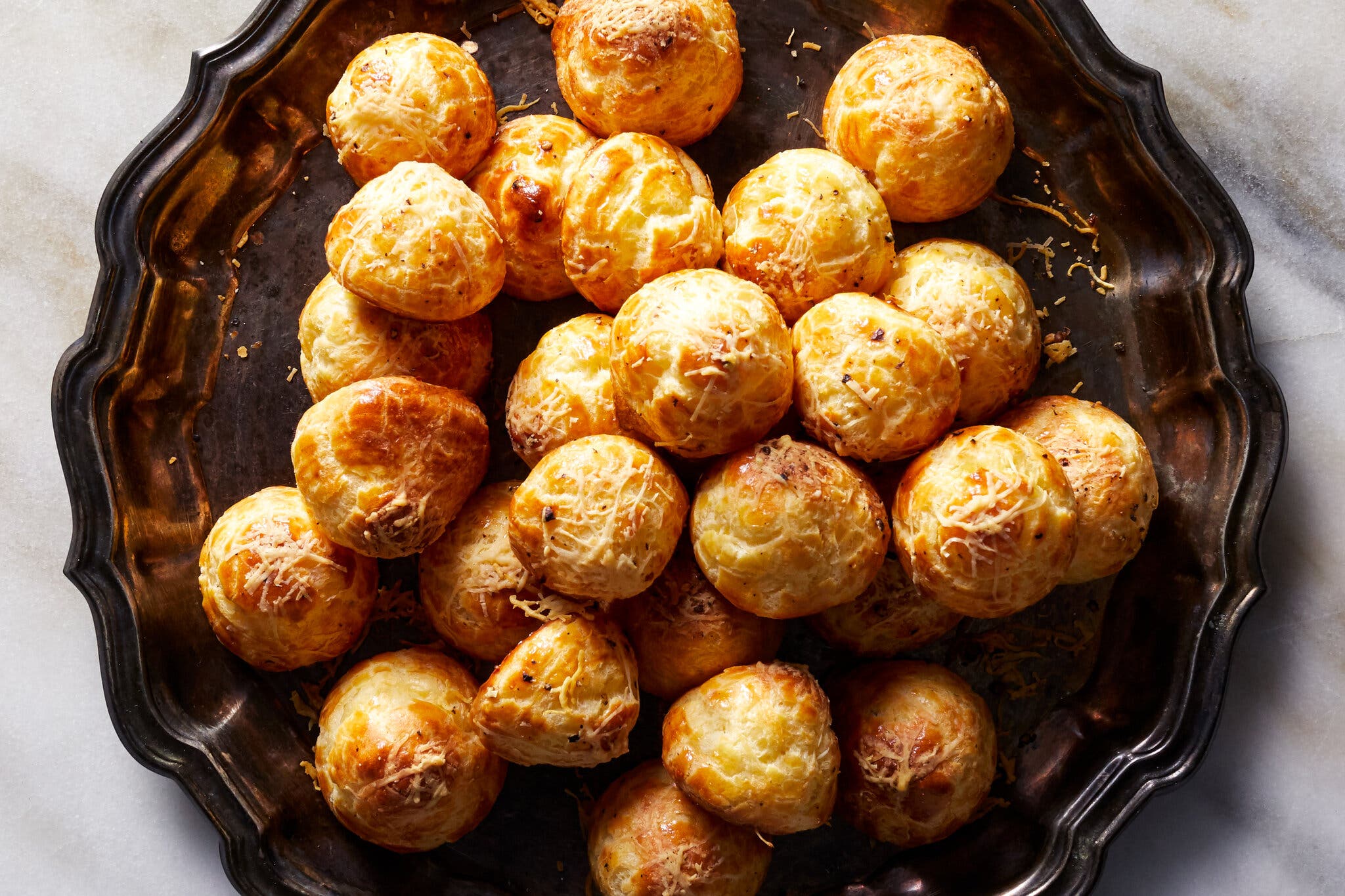 A pile of round, golden cheese puffs sits on a dark, decorative serving platter.