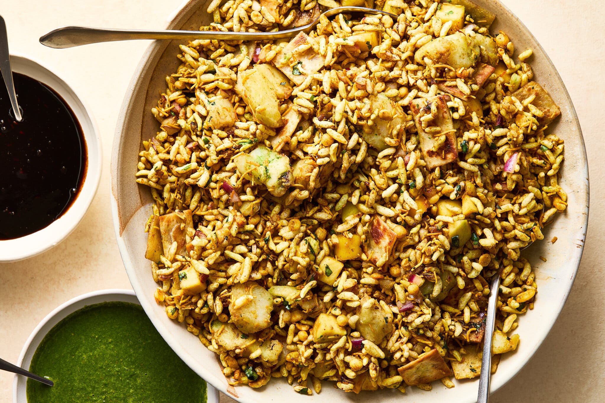 A golden-brown mix of puffed rice and vegetables fills a large bowl. Smaller bowls of dark brown and vibrant green sauces sit nearby.