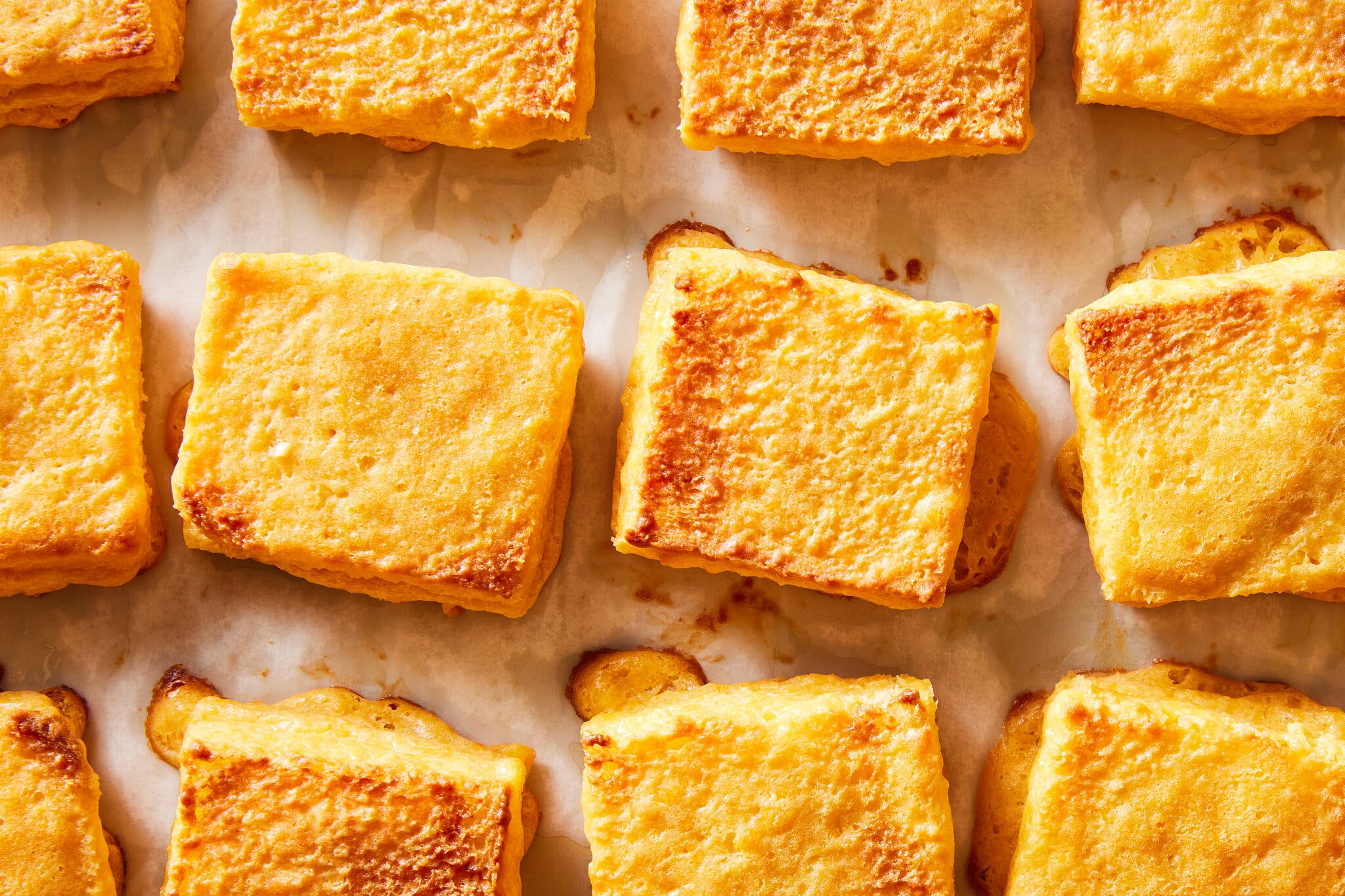 Golden-brown rectangular appetizers are arranged in rows on a light baking surface. They have slightly crispy edges and a soft, textured appearance.