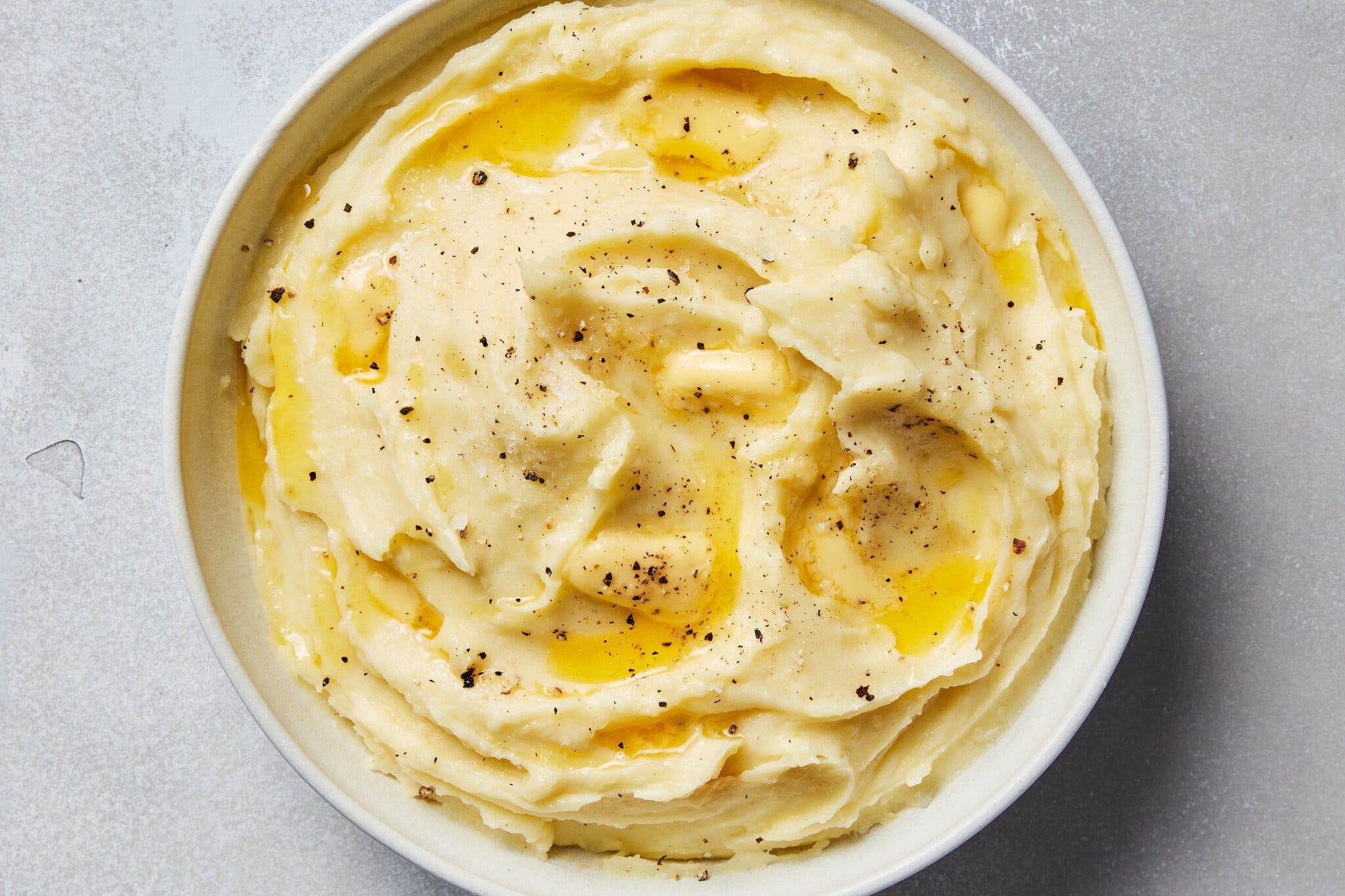 An overhead image of mashed potatoes topped with melting pats of butter and crushed black pepper.