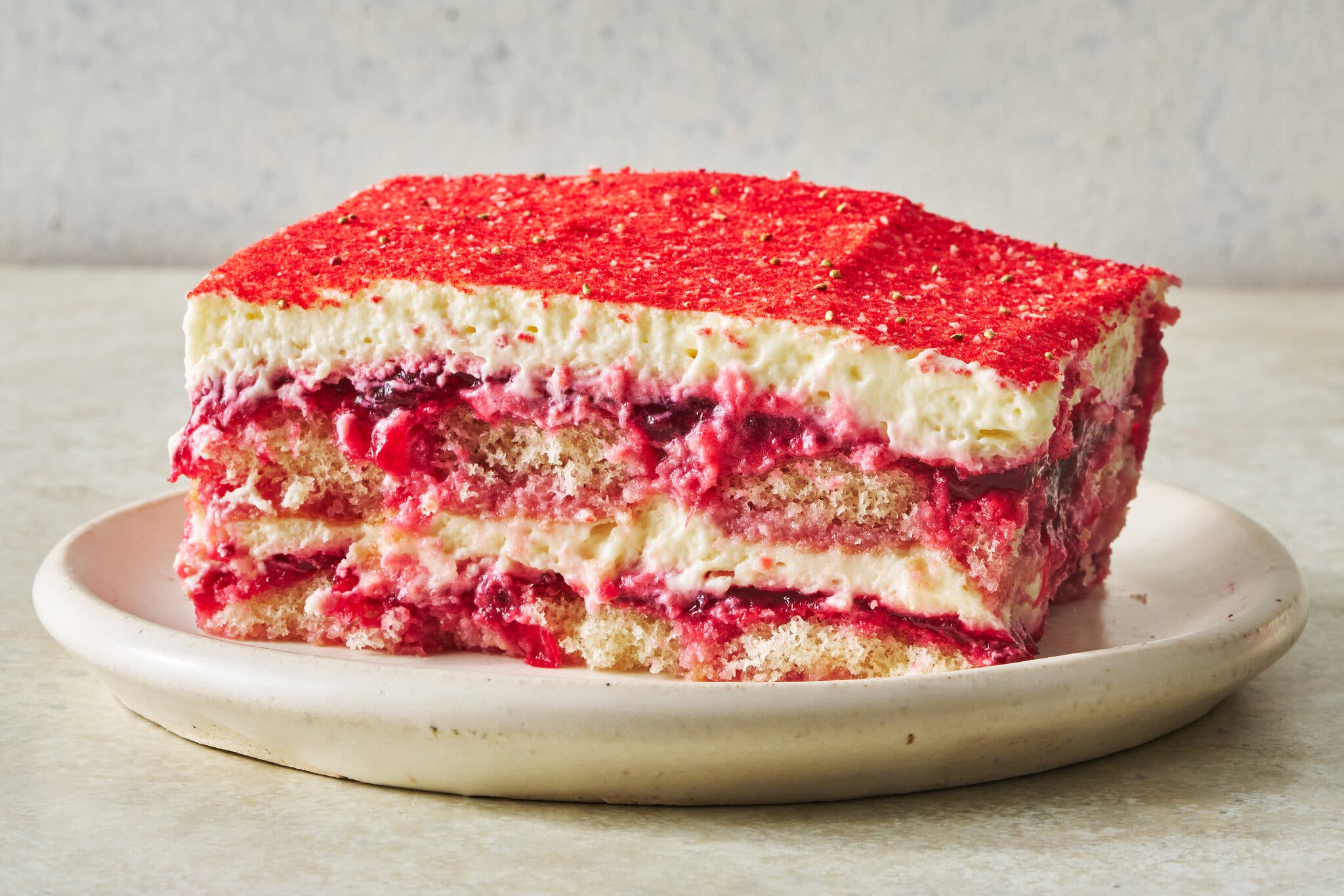 A square of red and white cranberry tiramisù sits on a stone plate.