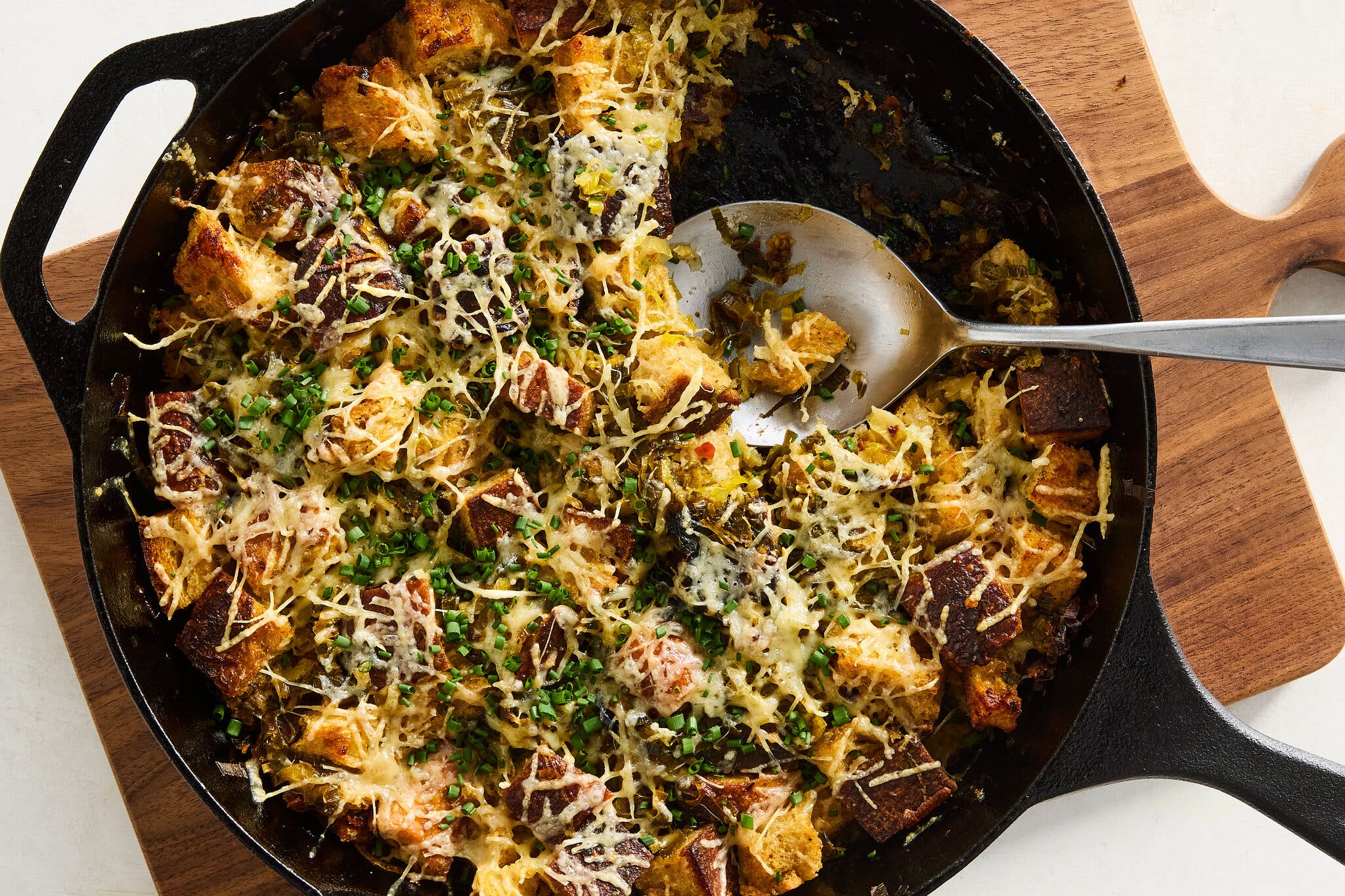 A black cast iron skillet holds bread pudding and a big silver spoon.