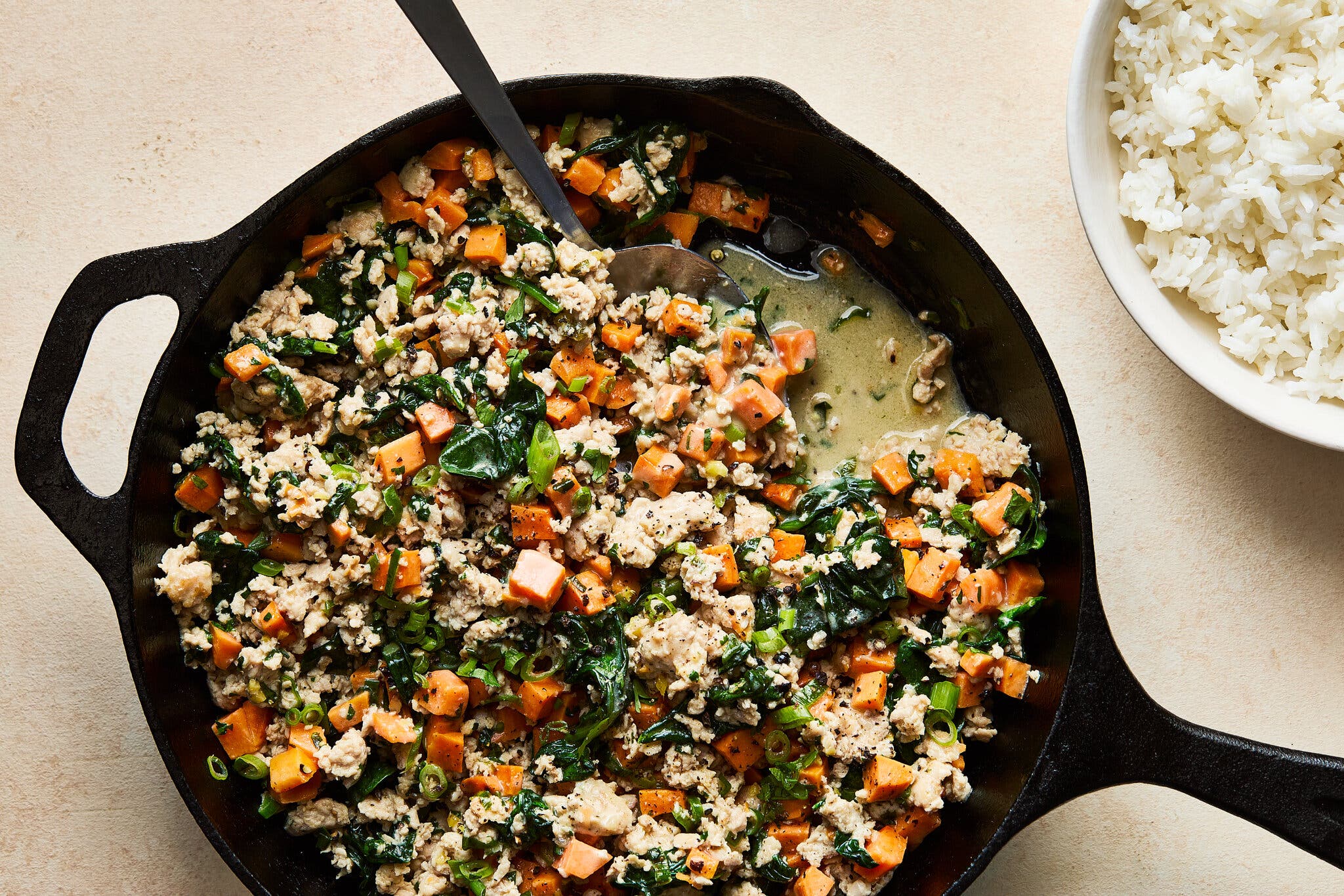 An overhead image of ground chicken mixed with sweet potato and herbs in a cast-iron skillet.