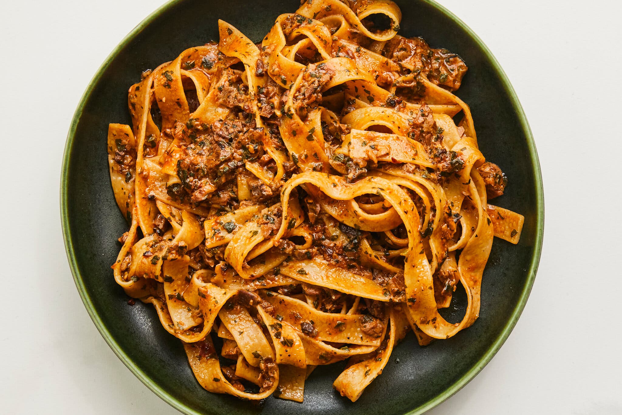 An overhead image of thick noodles tossed with a mushroom ragù in a green bowl.
