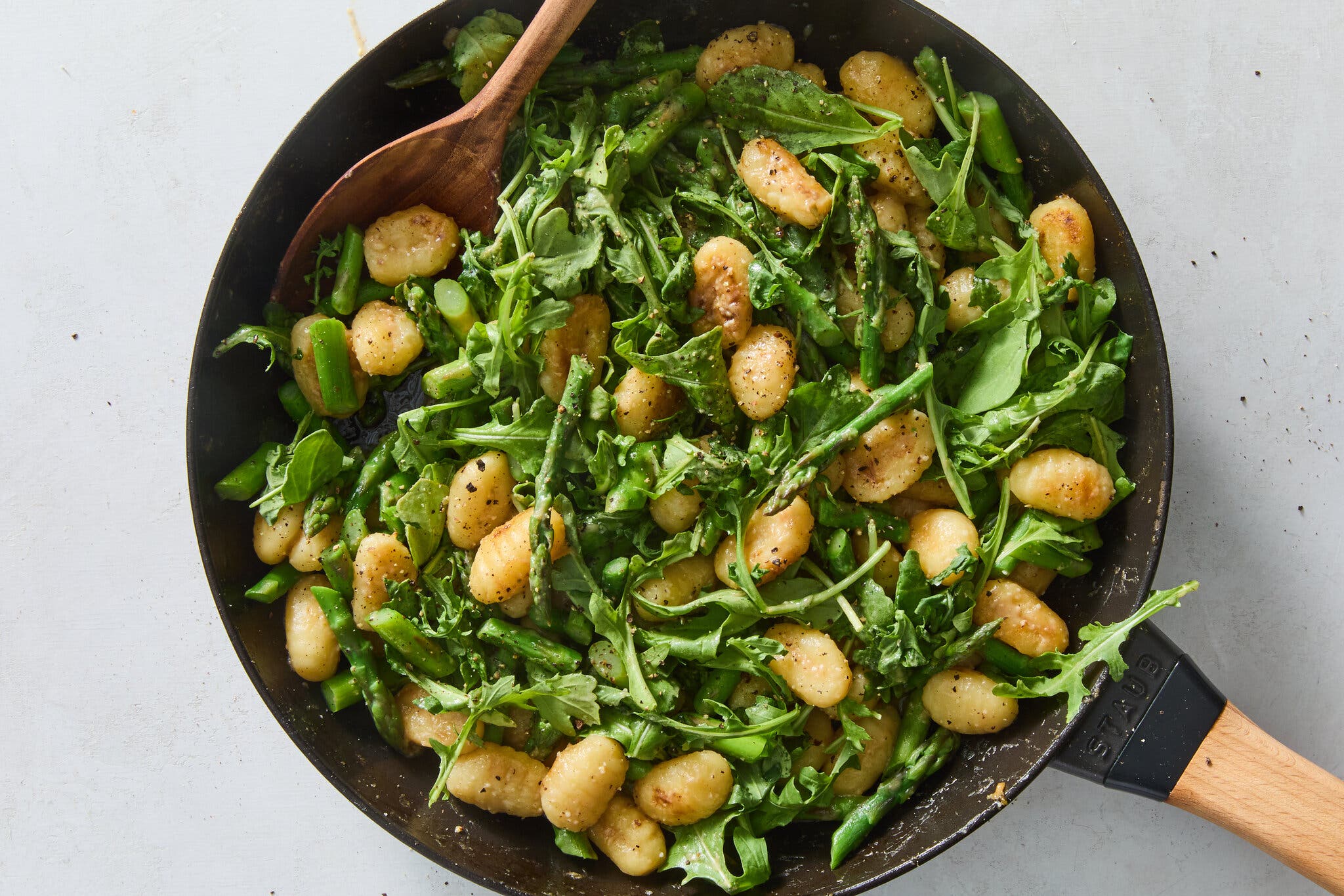 An overhead image of crisped gnocchi in a pan alongside asparagus and arugula.
