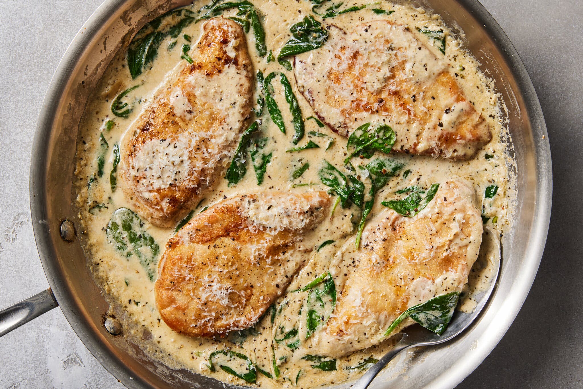 An overhead image of chicken breasts in a sauce studded with spinach.