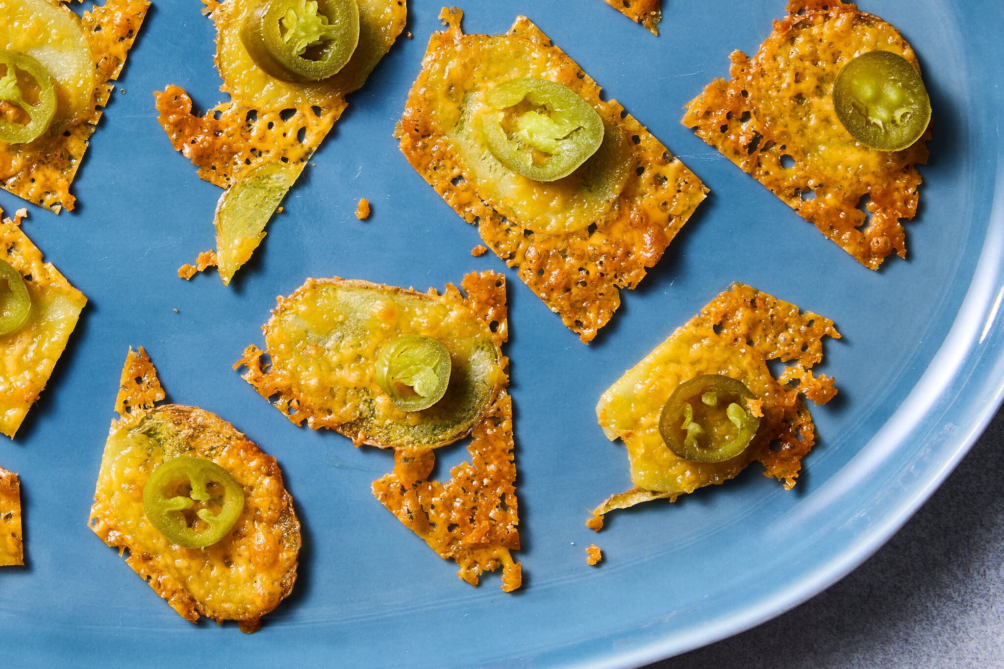A blue plate with cheese-and-potato crispy chips, each topped with a slice of pickled jalapeño