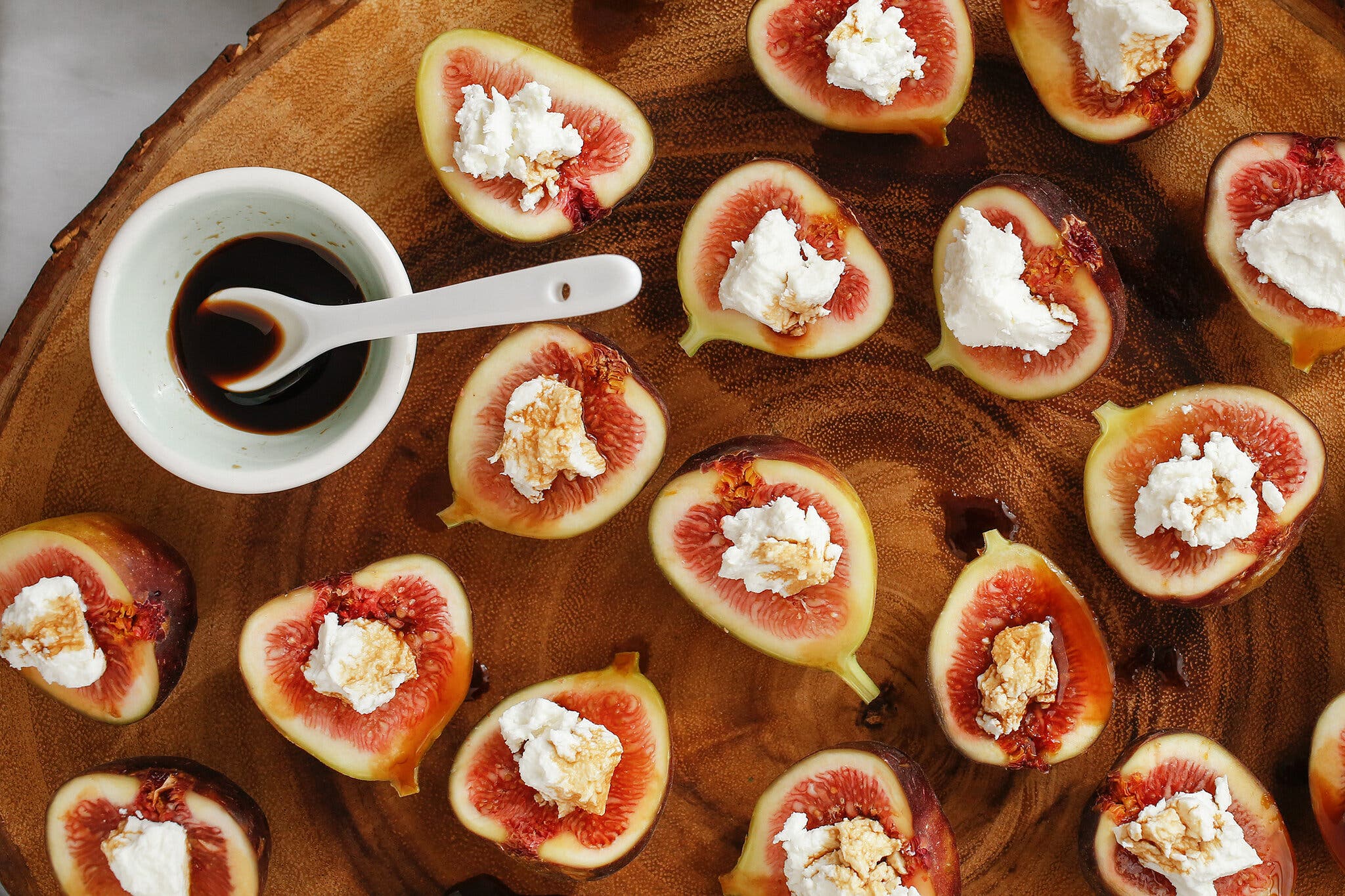 Figs stuffed with goat cheese arranged on a wooden serving board. There is a small dish of balsamic vinegar on it.