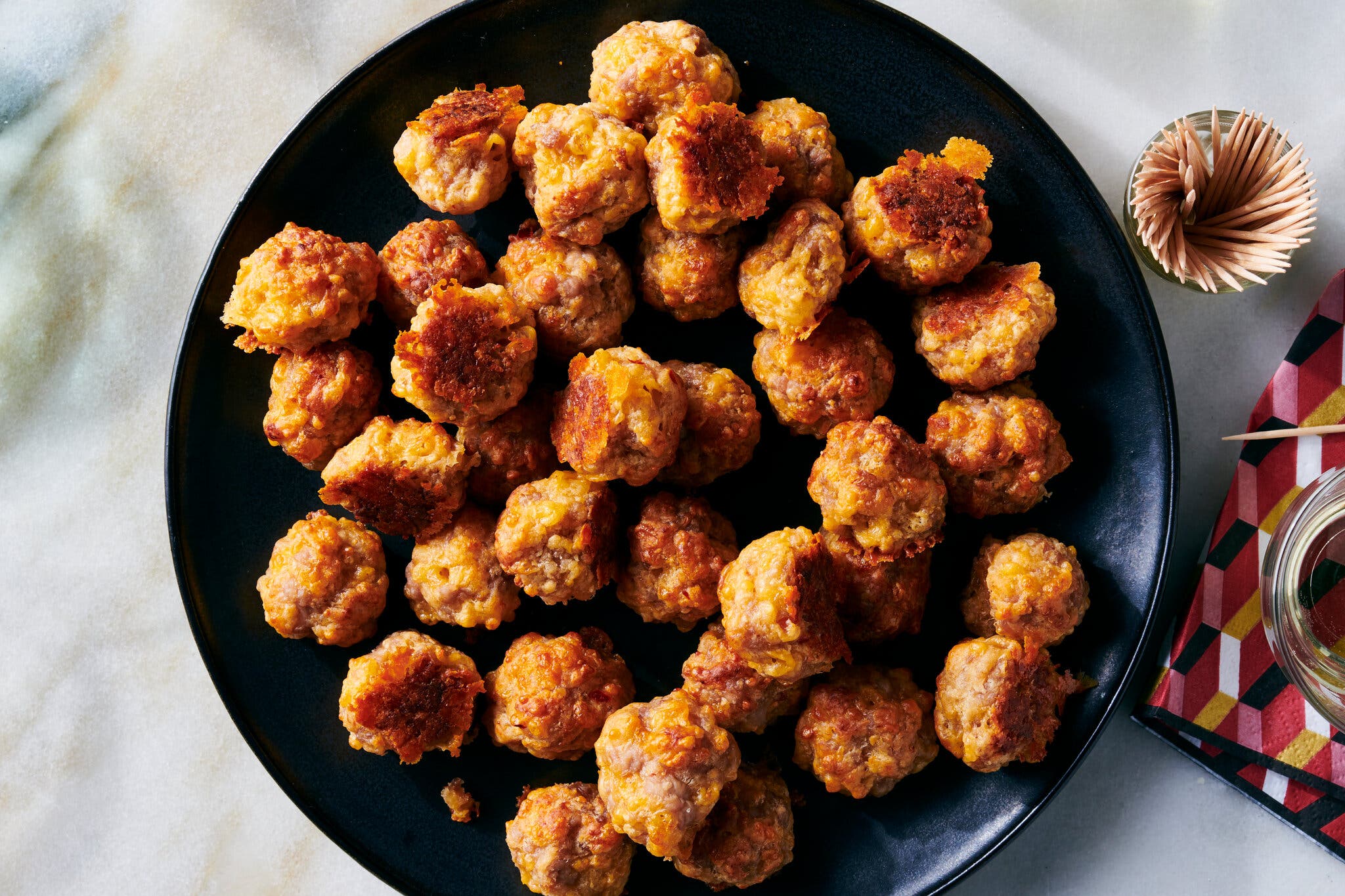 A large black plate of sausage balls, with a small cup of toothpicks to the right.