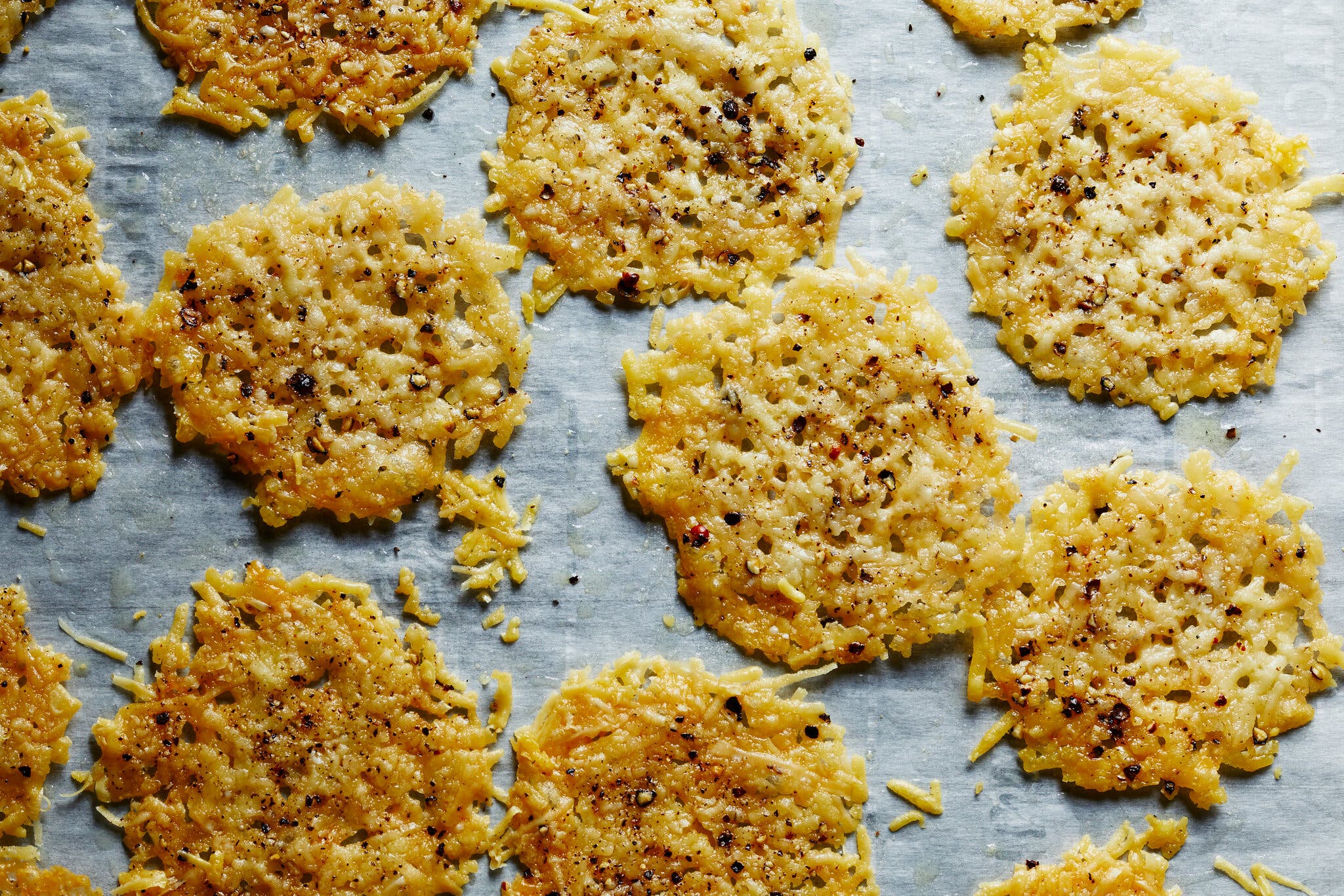 Crispy cheese crackers arranged on parchment paper, each topped with cracked black pepper.