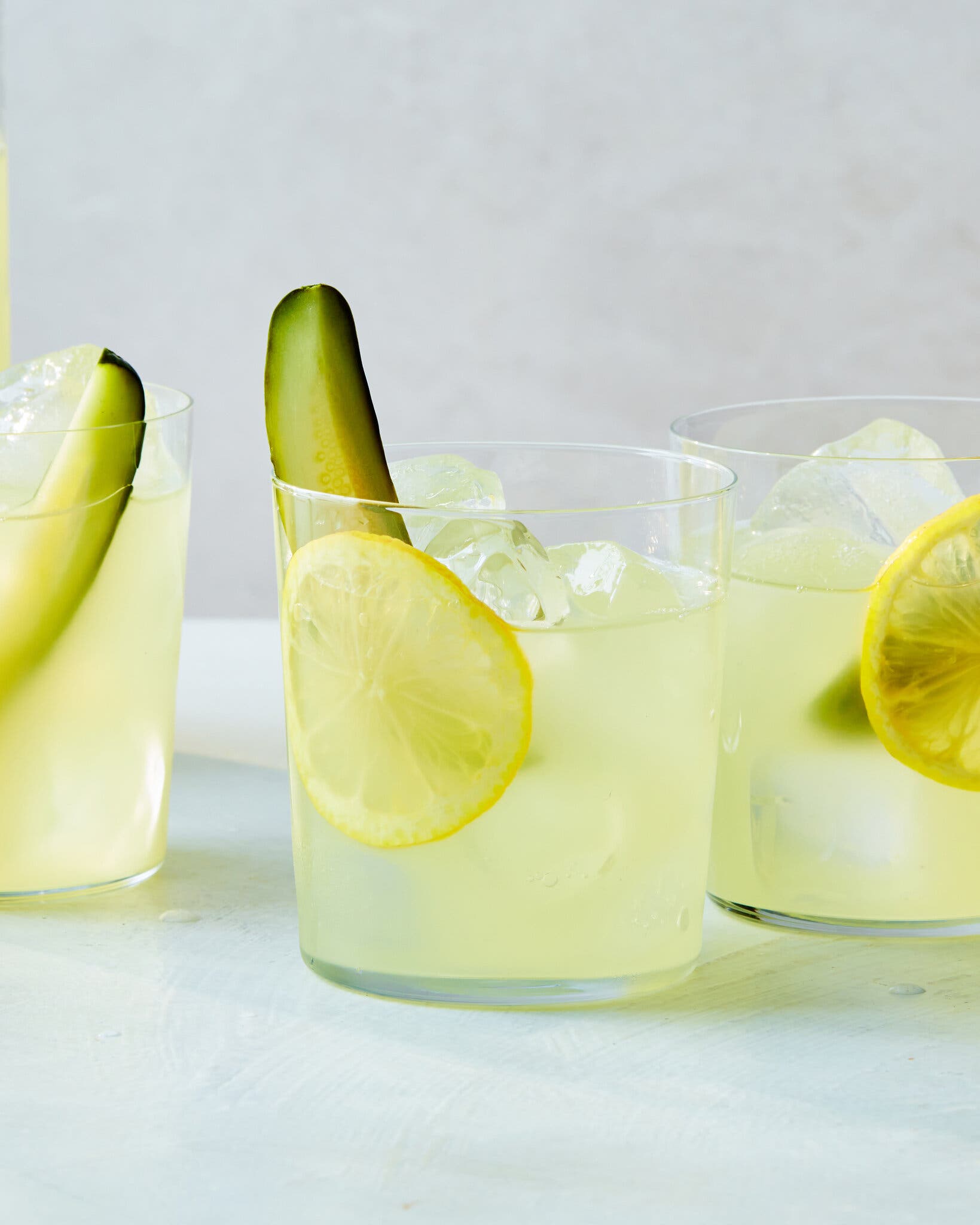 Three glasses of lemonade are filled with ice, lemon slices and pickle spears.