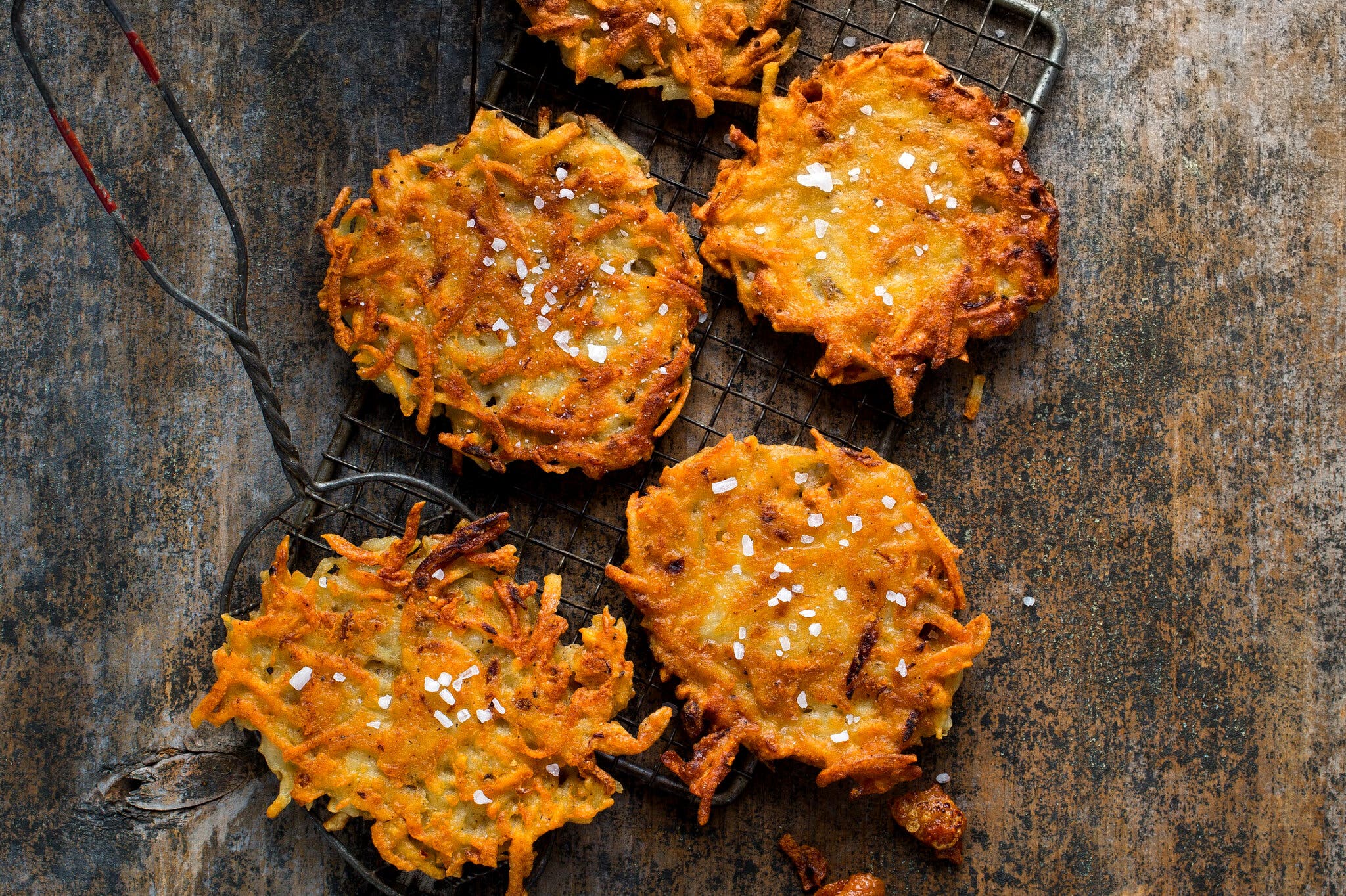 A wire cooling rack with several latkes it, alongside a latke on a spatula.