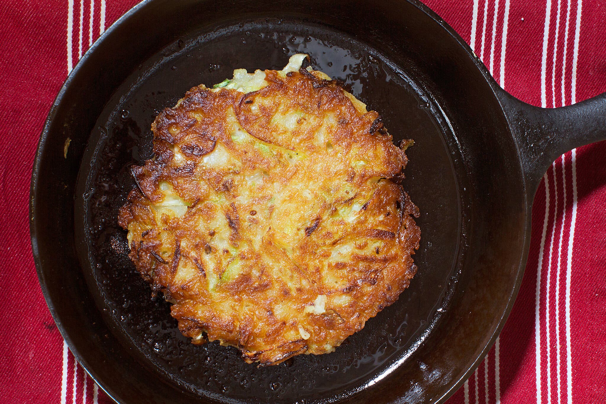 A cast-iron skillet with a potato pancake that includes cabbage and bean sprouts.