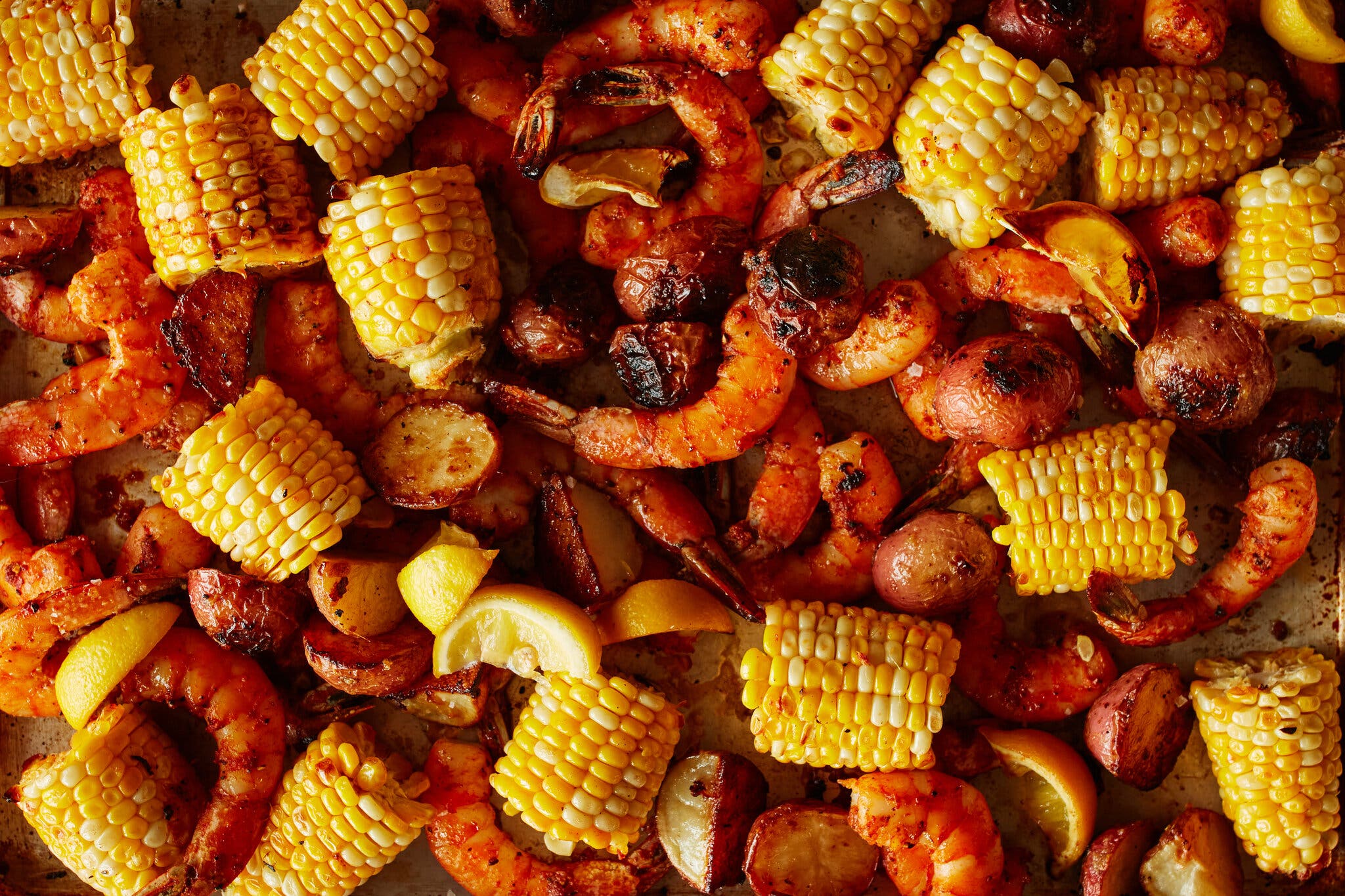 Shrimp, corn and potatoes are spread on a sheet pan.